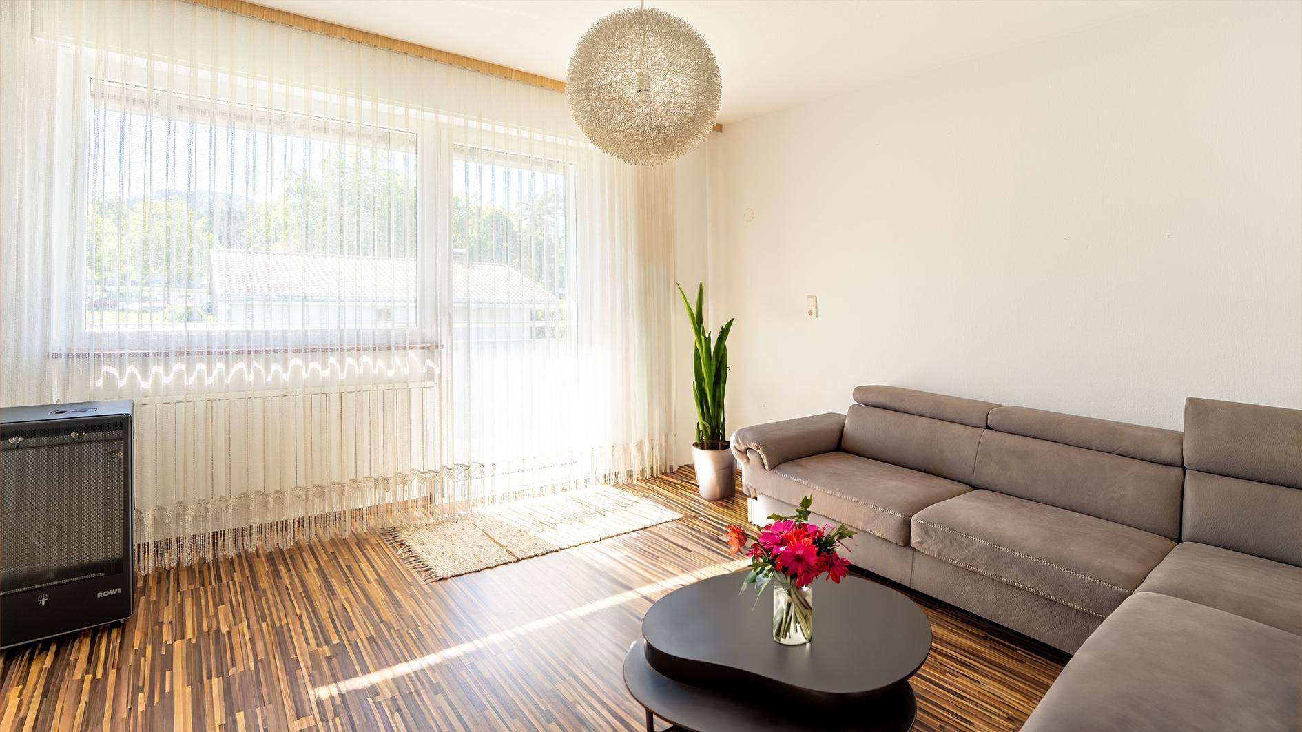 Geräumiges Wohnzimmer mit Holzboden, großem Sofa und viel Tageslicht.