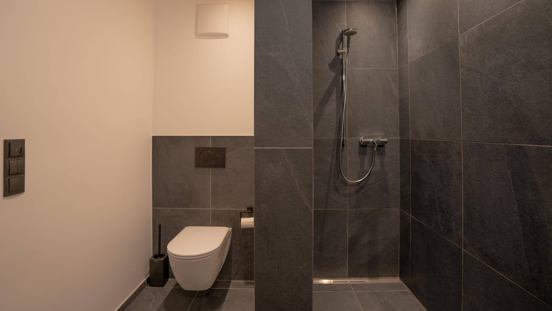 Modernes Badezimmer mit dunklen Fliesen, wandhängendem WC und ebenerdiger Dusche.