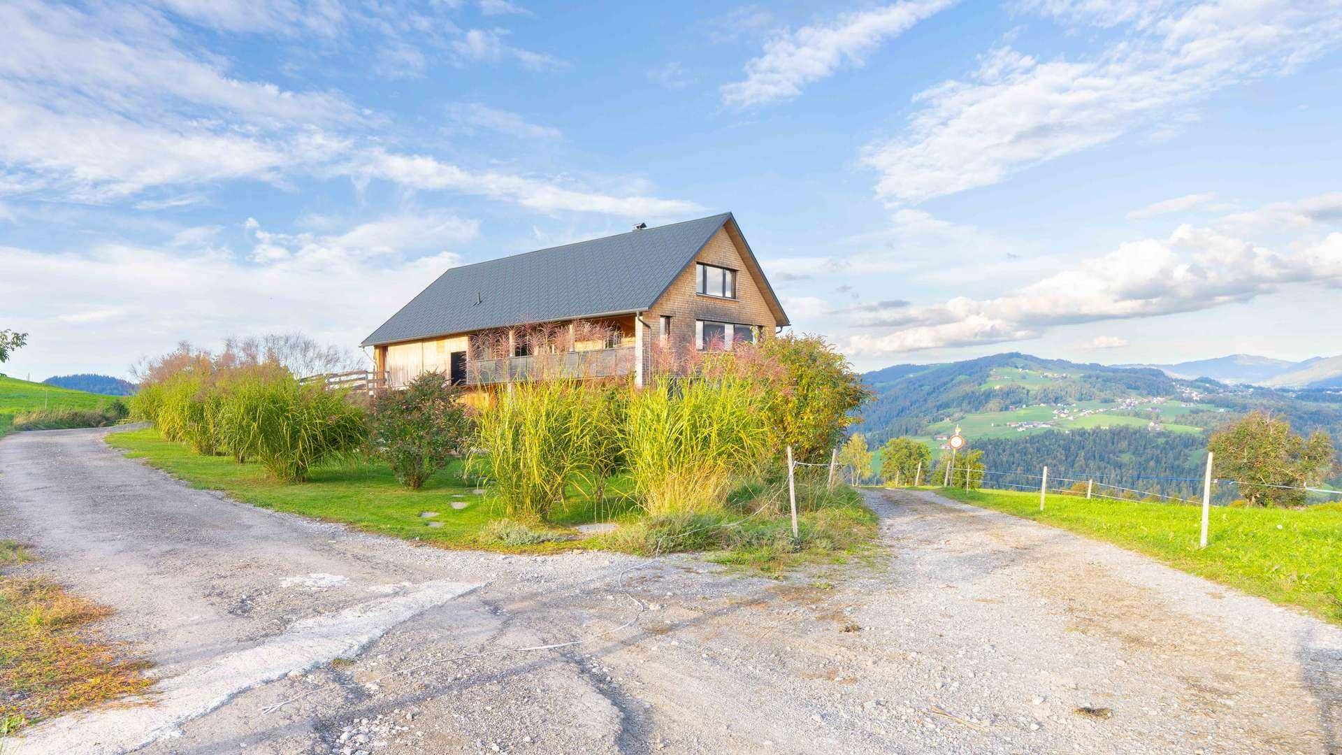 Modernes Holzhaus in ländlicher Umgebung mit Zufahrtswegen und weitem Blick auf die Berge.