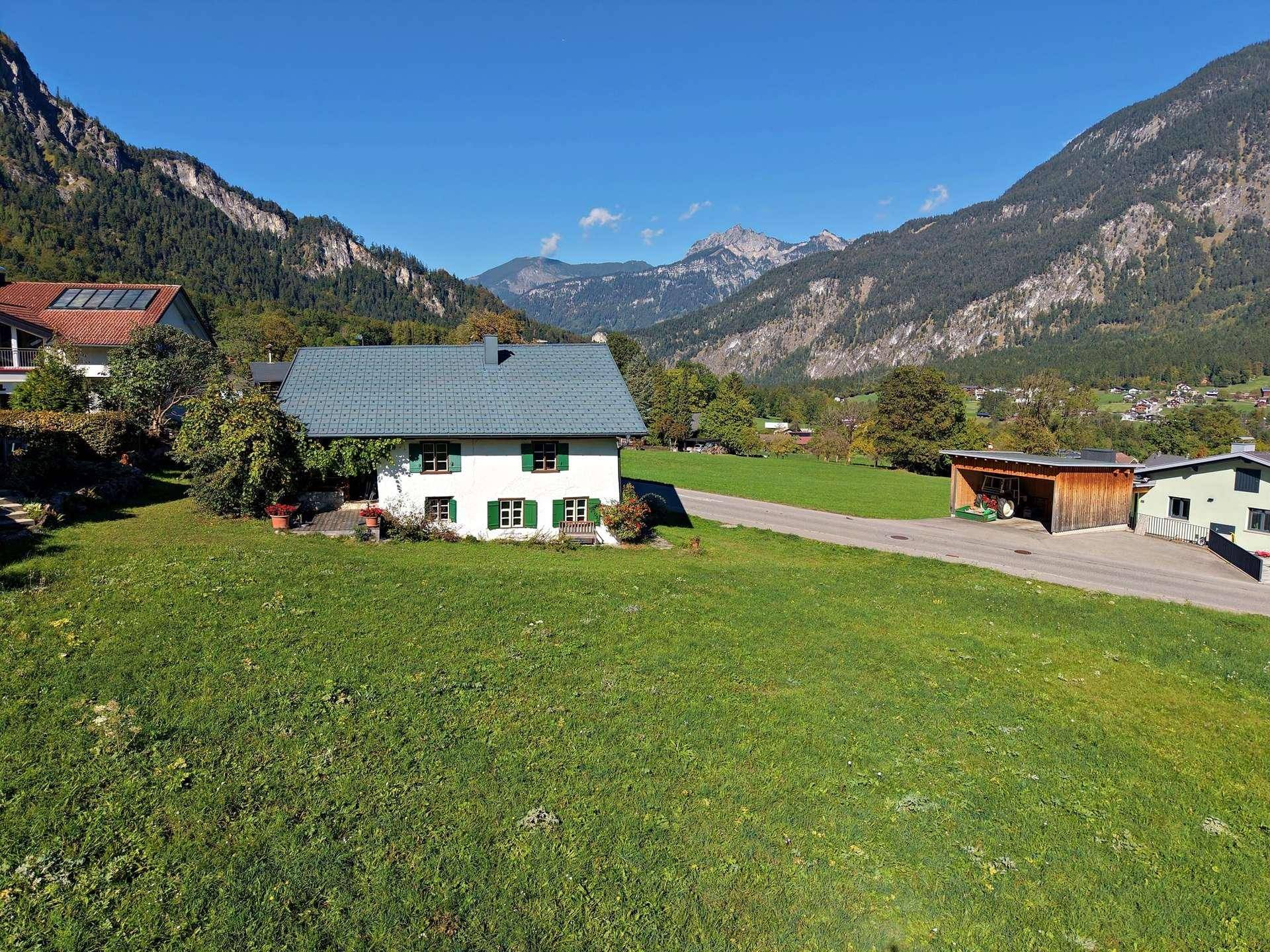 Traditionelles Haus mit grünen Fensterläden und Satteldach vor beeindruckender Bergkulisse.