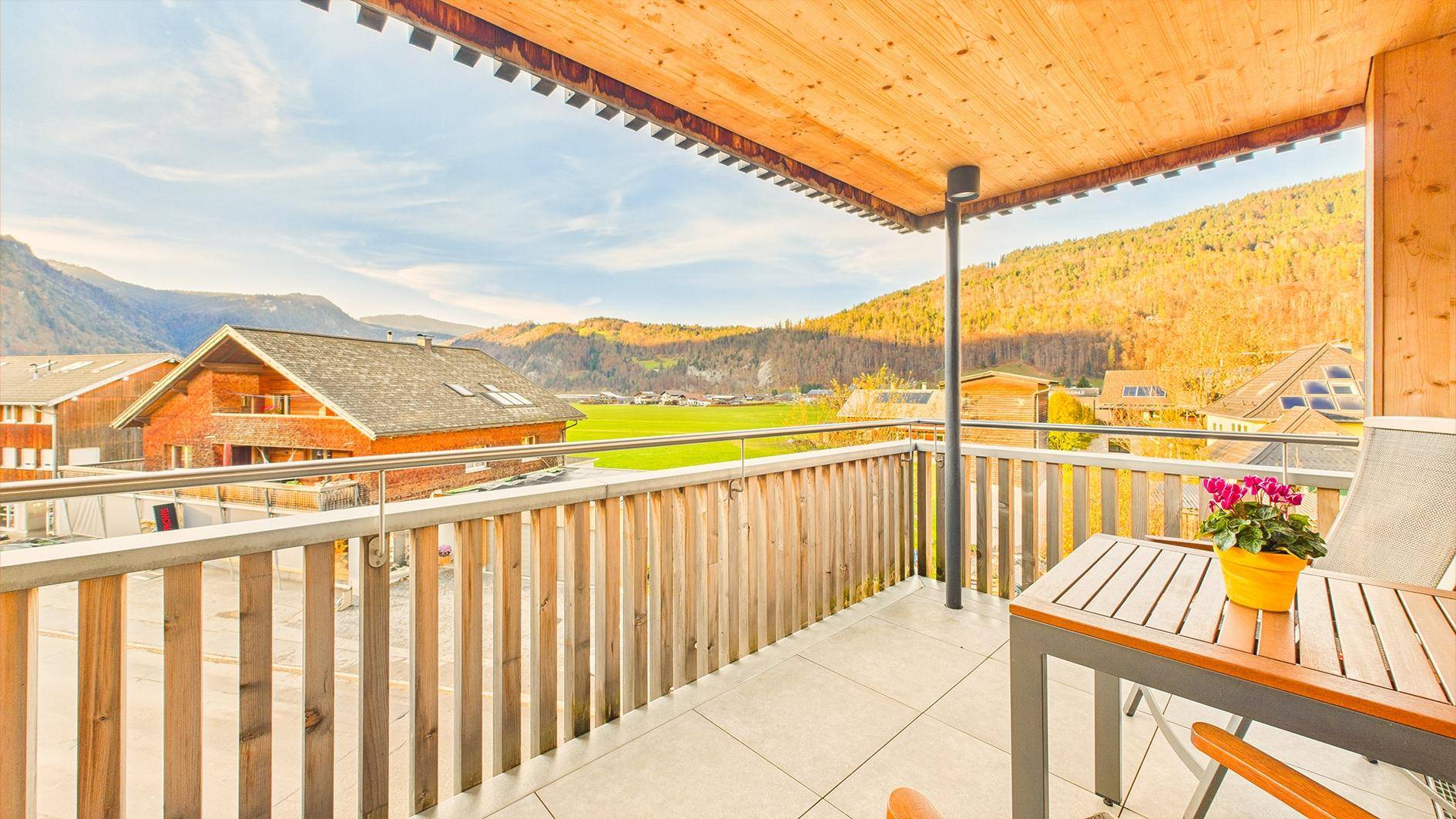 Geräumiger Balkon mit Holzelementen, Fliesenboden und Panoramablick auf die Berge und Natur.