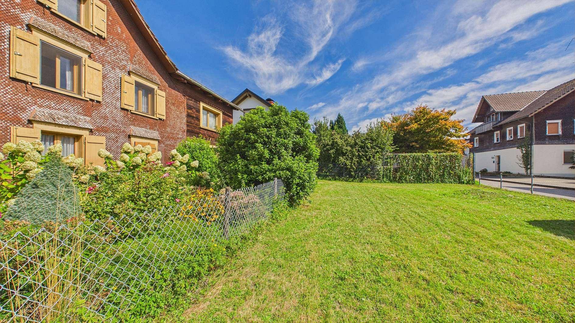 Gartenbereich mit Rasenfläche und Blick auf die traditionelle Hausfassade mit Fensterläden.