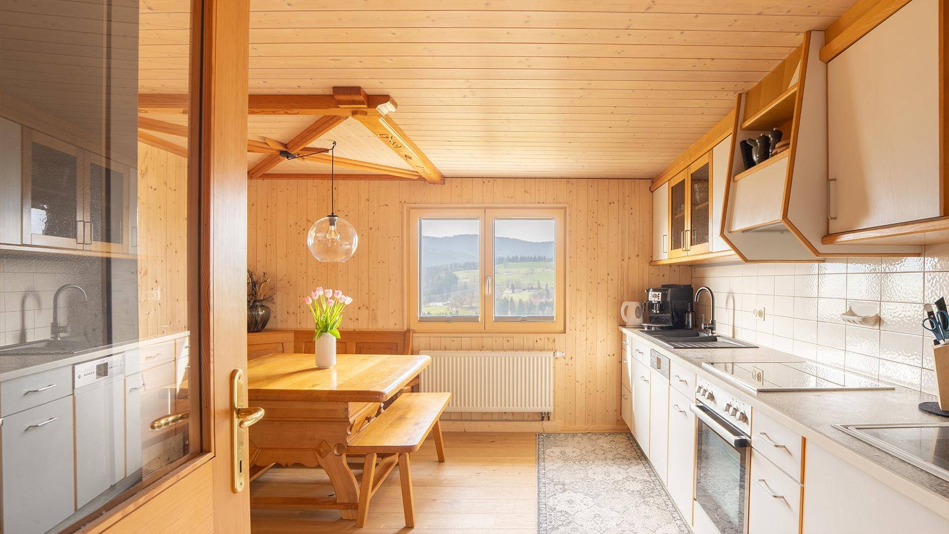 Rustikale Wohnküche mit Holzvertäfelung, Essbereich und Blick auf die Landschaft.