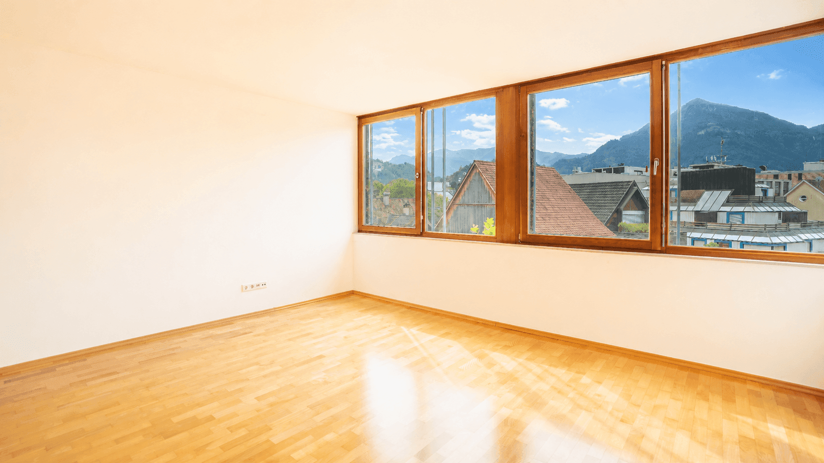 Geräumiges Schlafzimmer mit Holzboden und weitem Blick auf die Berge und die Dächer der Stadt.