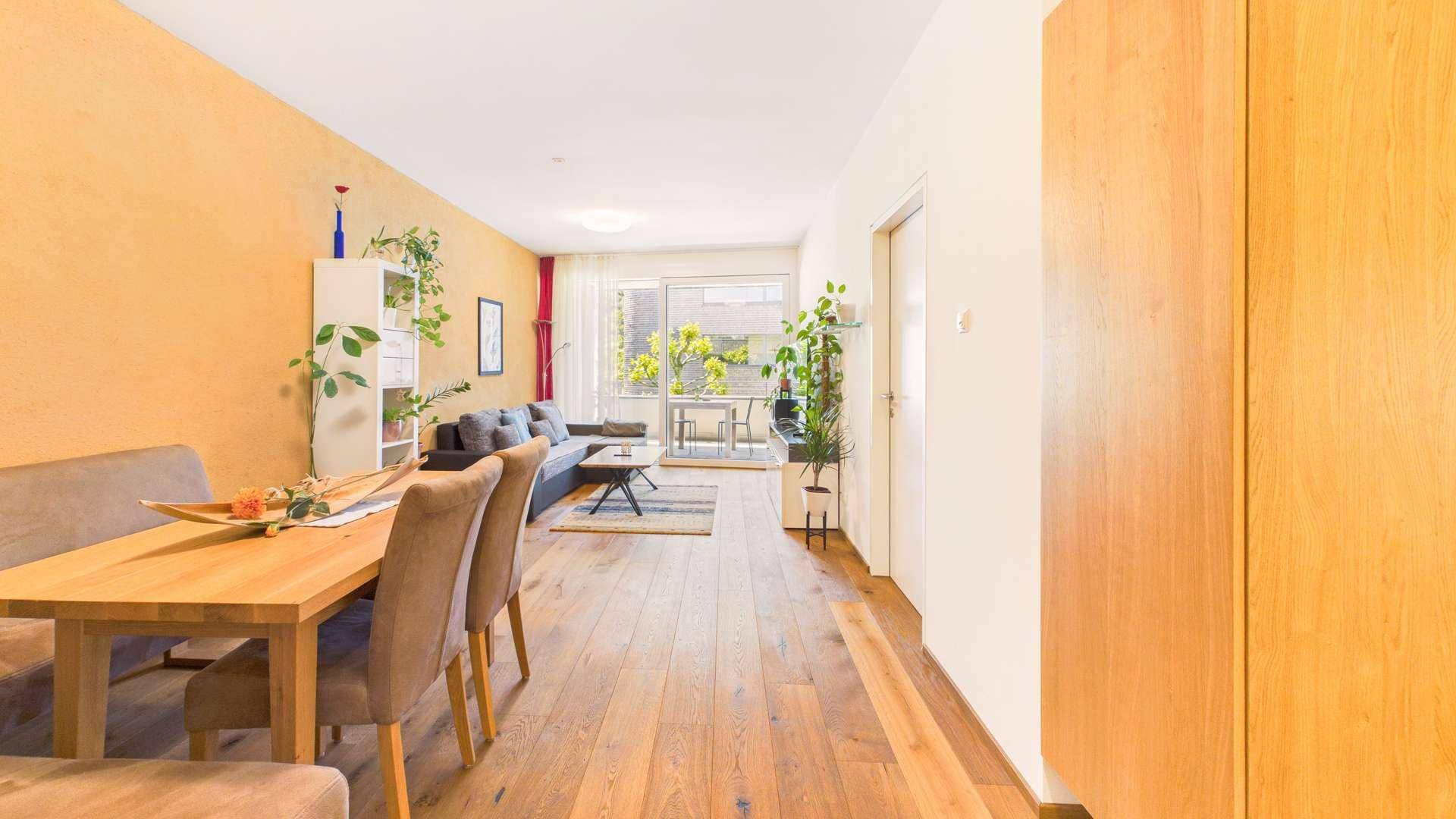 Offener Wohn- und Essbereich mit Holzboden, gelber Wand und Zugang zum Balkon.