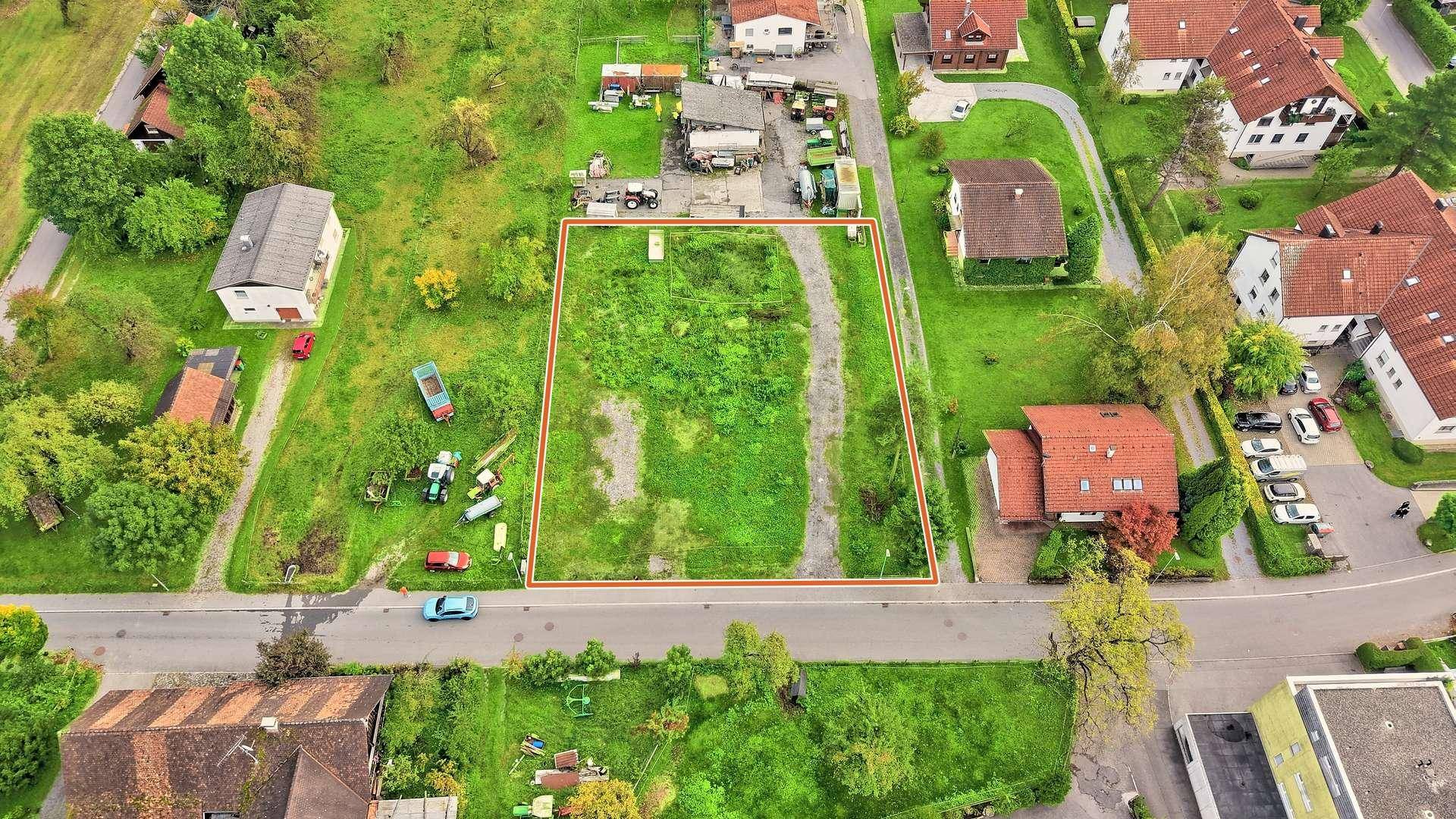 Luftaufnahme eines weitläufigen, grünen Grundstücks, das von einer Straße und mehreren Wohnhäusern umgeben ist.