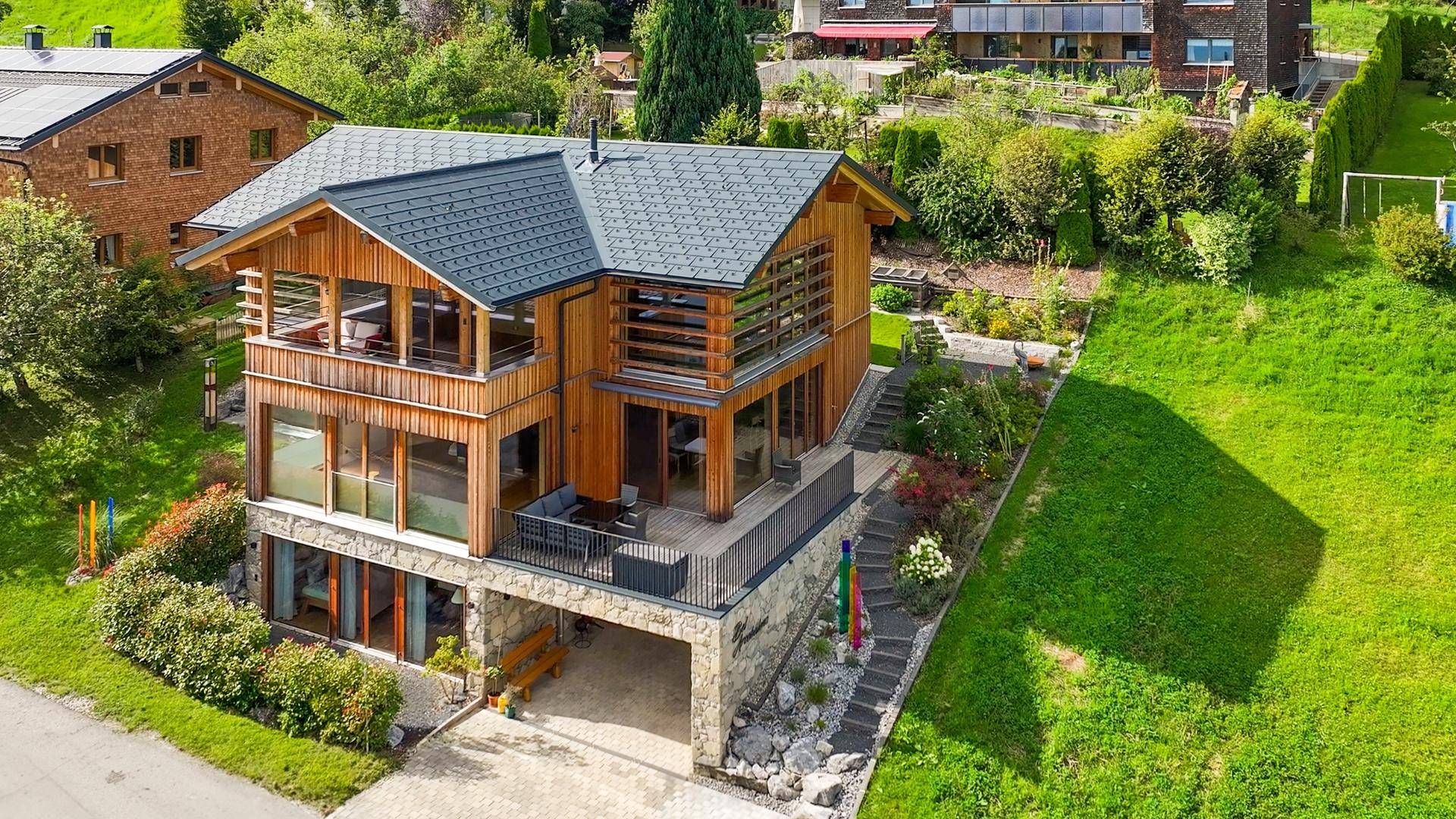 Luftaufnahme des modernen Holzhauses mit Satteldach und weitläufigem Grundstück in Hanglage.