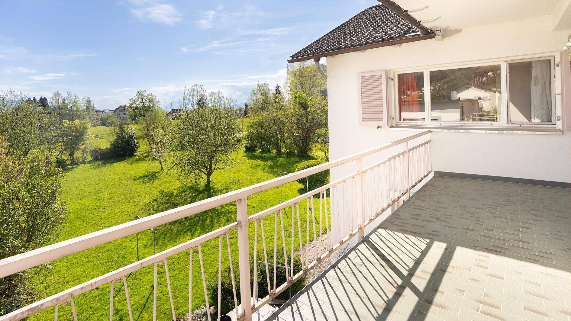 Großer Balkon mit Fliesenboden und weitem Blick über die grüne Landschaft.