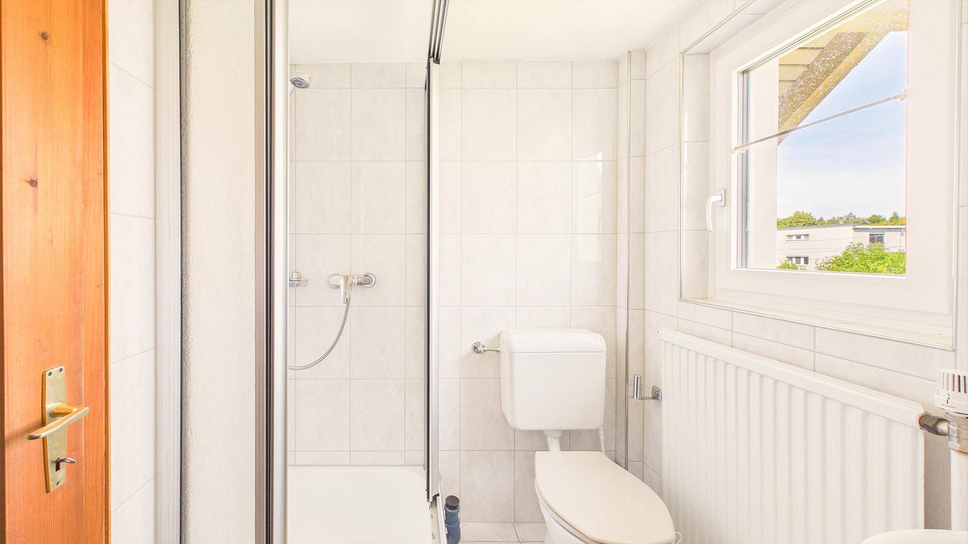 Funktionales Badezimmer mit Duschkabine, WC, Heizkörper und Fenster für Tageslicht.