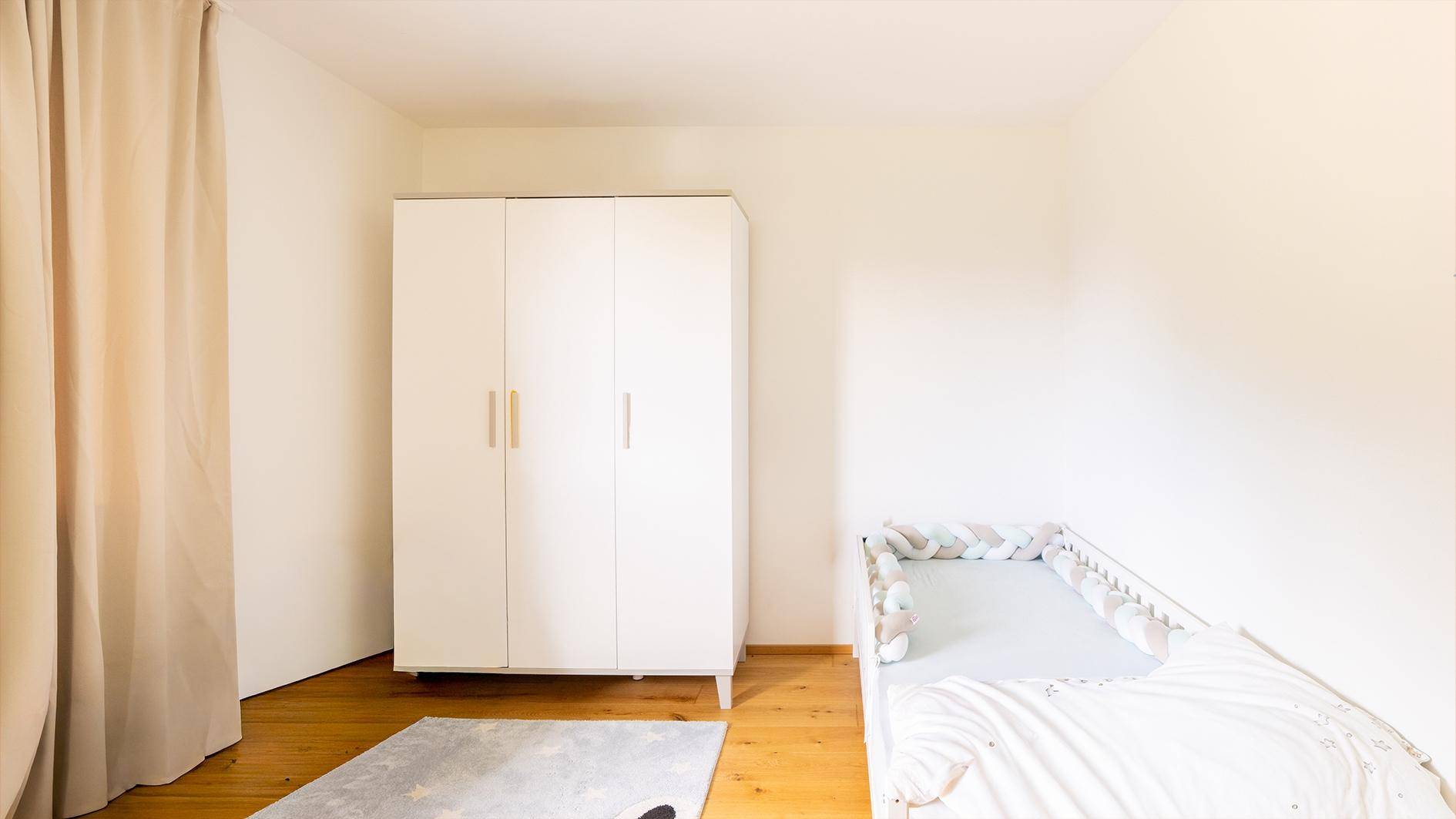 Kinderzimmer mit weißem Kleiderschrank, Babybett und hellem Parkettboden.