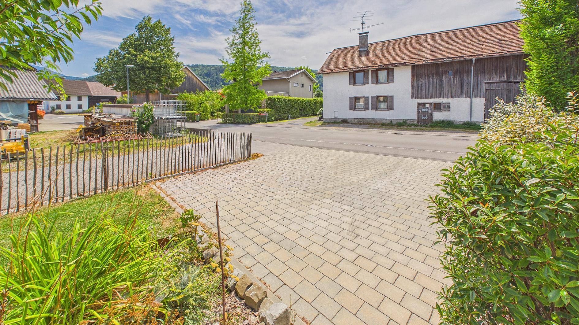 Gepflasterte Einfahrt zum Haus, umgeben von grünen Pflanzen und Büschen.