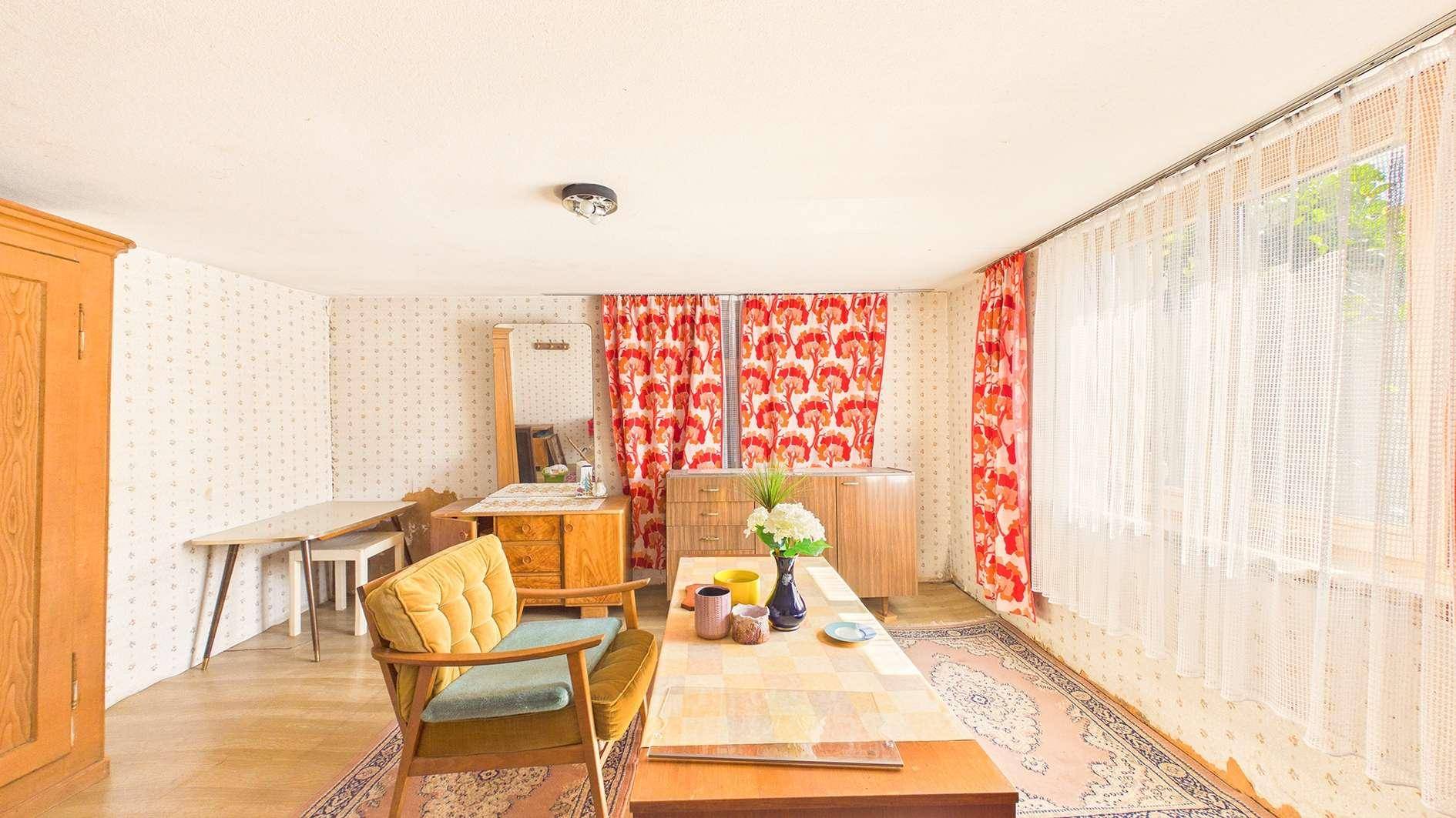 Raum mit Vintage-Möbeln, gemusterten Tapeten und roten Blumenmustervorhängen.