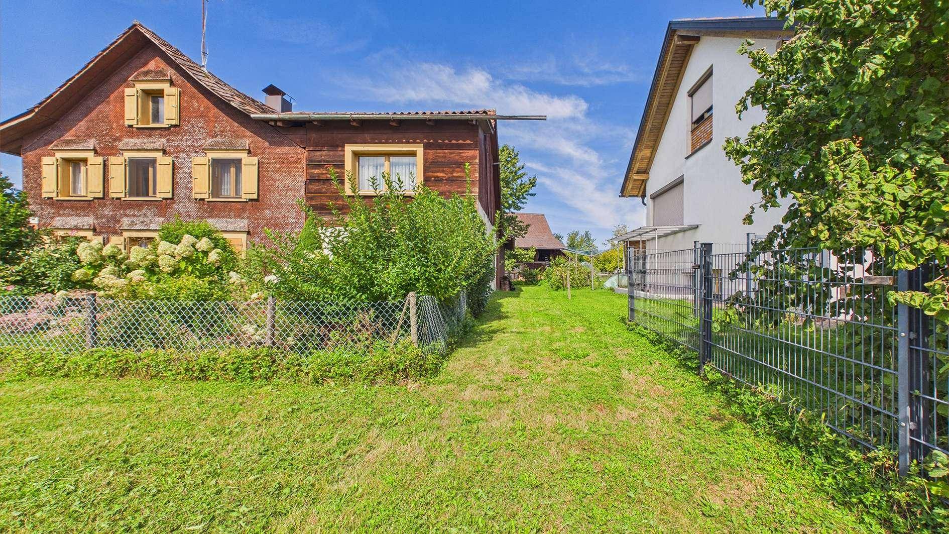 Grüner Gartenweg zwischen zwei Häusern unter blauem Himmel mit leichter Bewölkung.