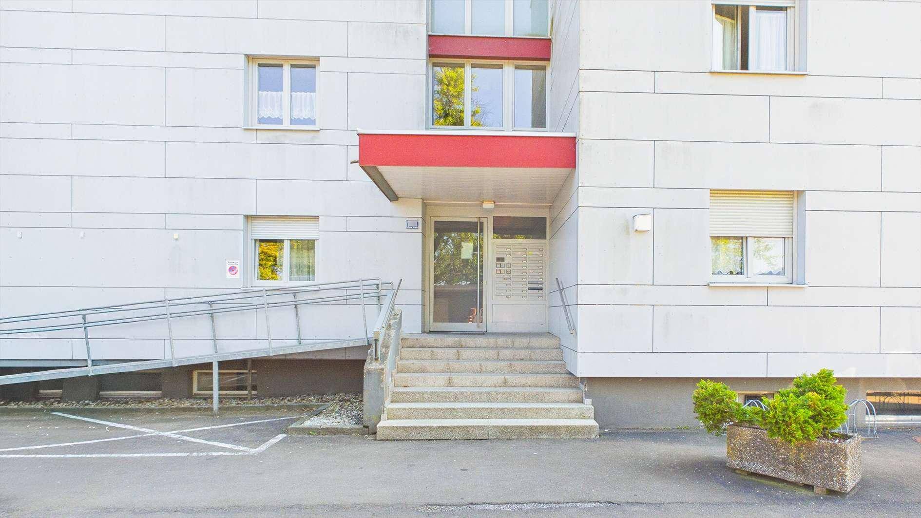 Eingangsbereich eines Mehrfamilienhauses mit Treppe und barrierefreier Rampe.