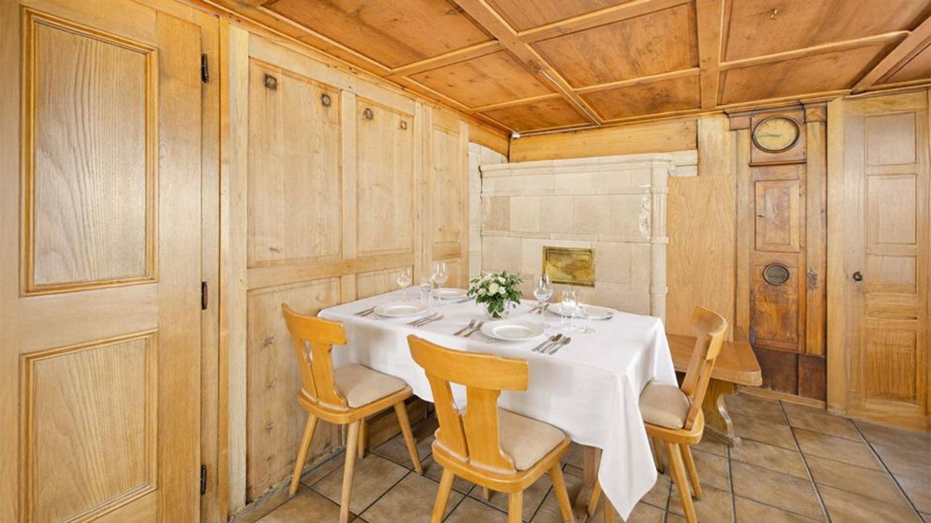 Gemütlicher Essbereich mit Kachelofen, Holztäfelung und rustikalen Holzstühlen.