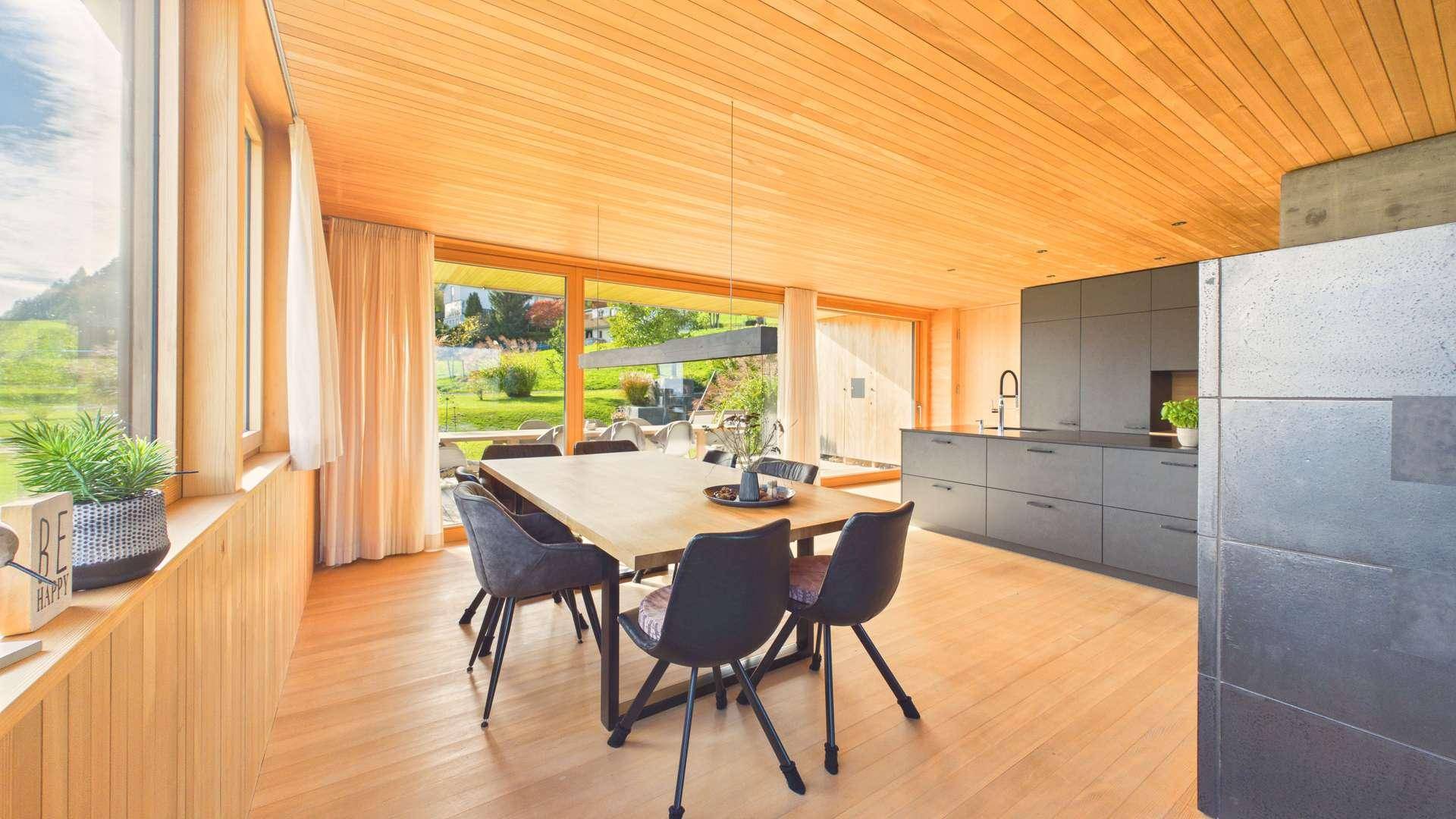Heller offener Wohn-Essbereich mit Holzboden, moderner Küche und großen Fenstern zur Landschaft.