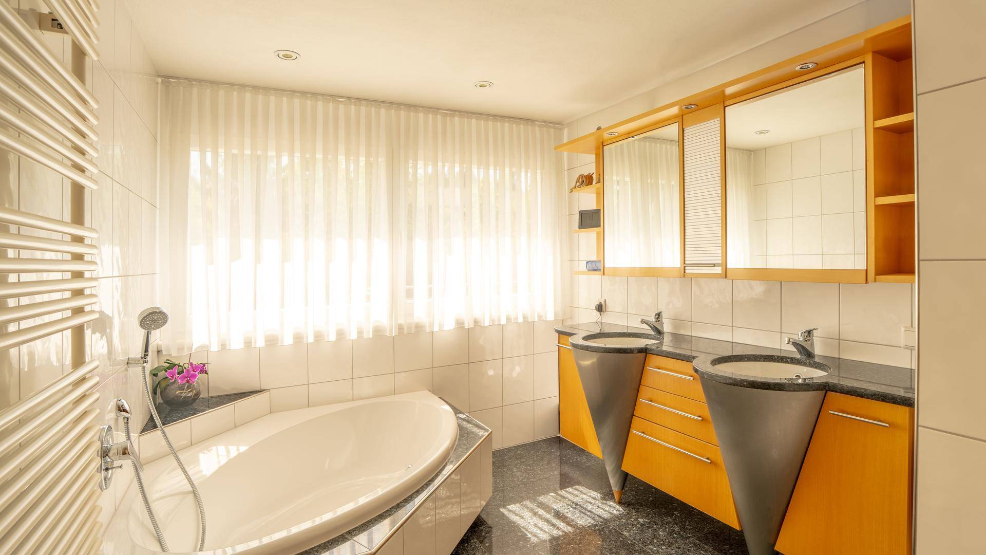 Geräumiges Badezimmer mit Badewanne, Doppelwaschbecken und großem Fenster für Tageslicht.