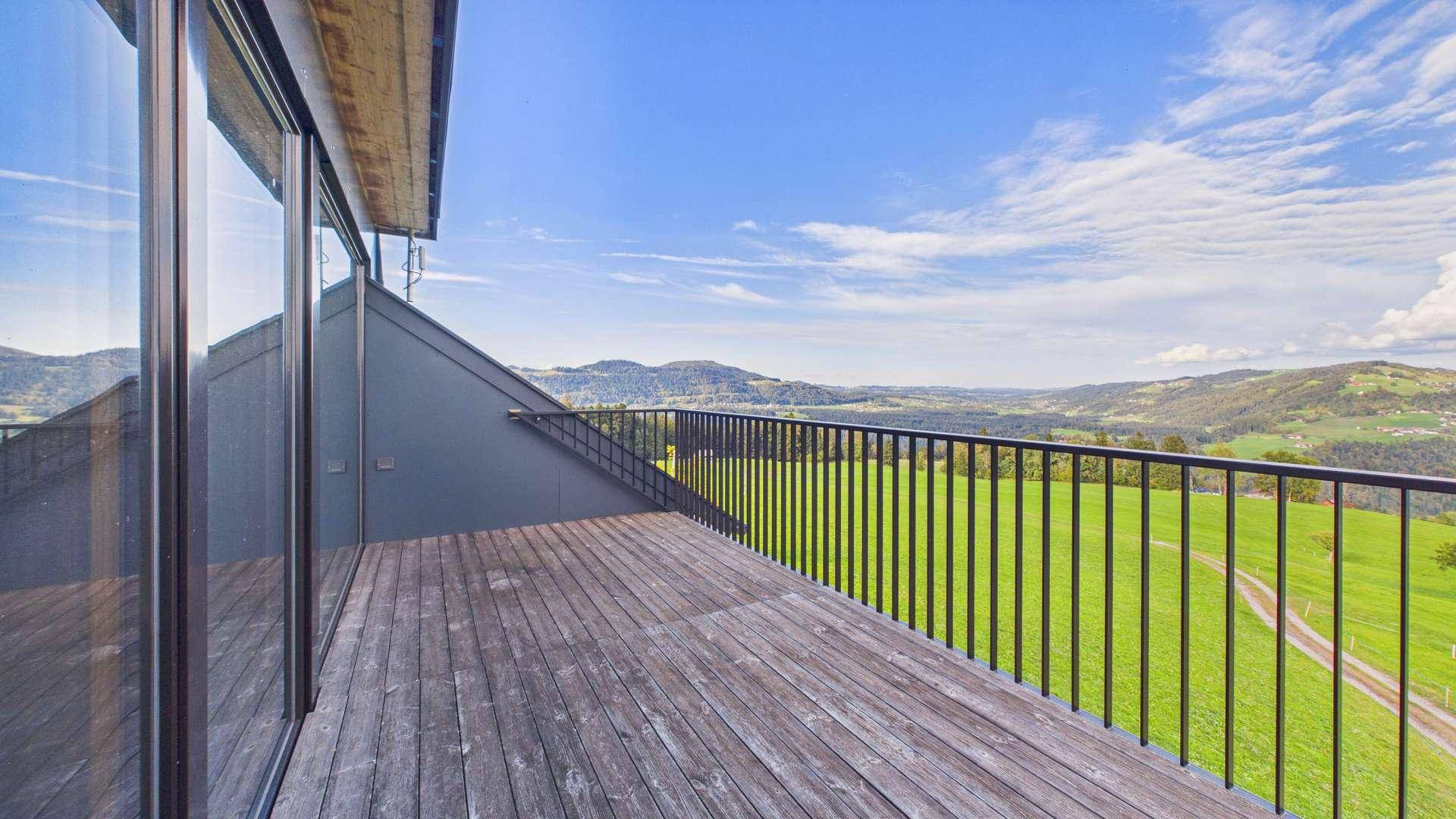 Großer Balkon mit Holzboden und Metallgeländer, bietet einen weiten Blick auf die grüne Landschaft.