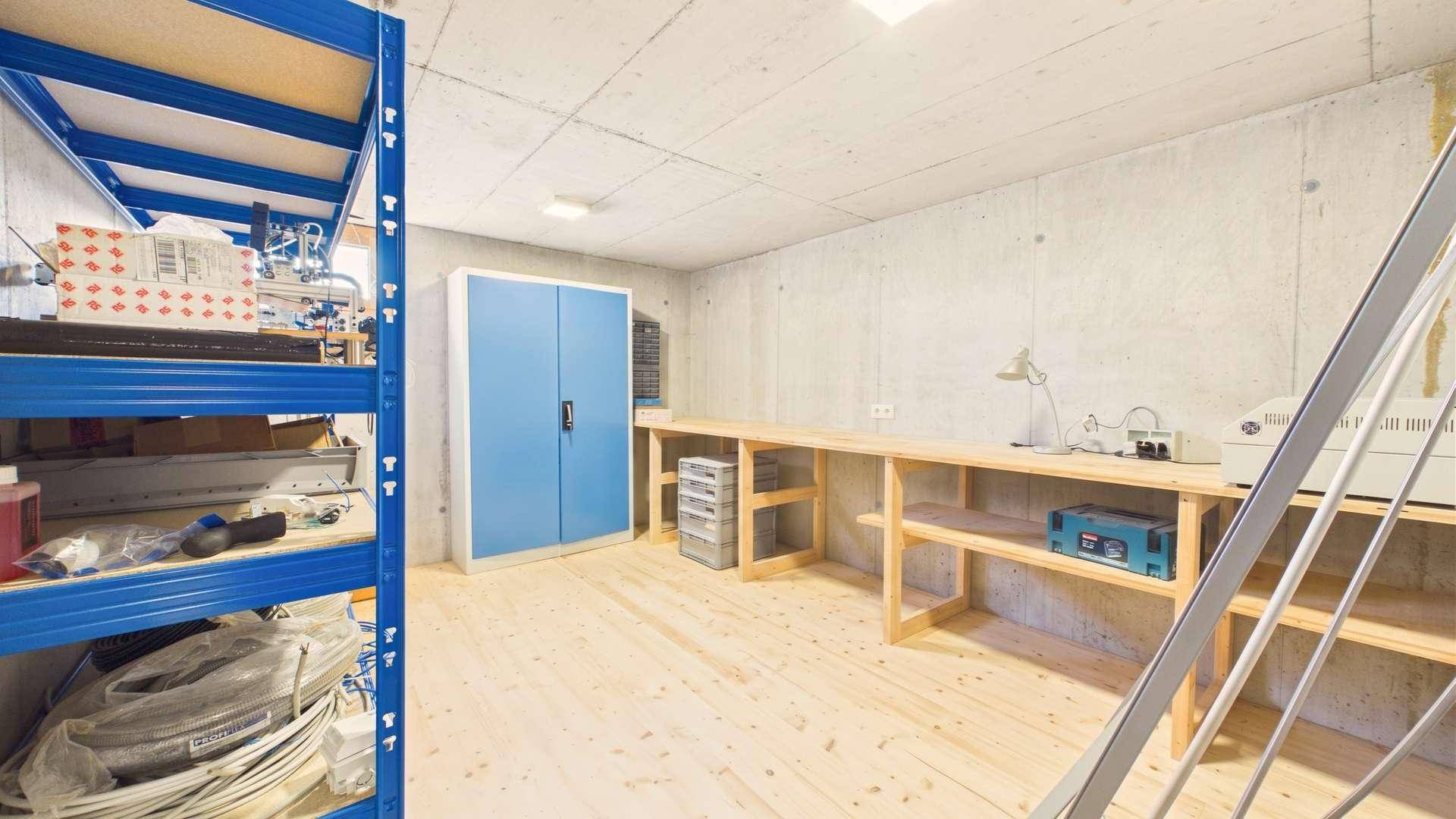Geräumiger Werkstattbereich im Keller mit Holzboden, Werkbänken und blauen Lagerschränken.