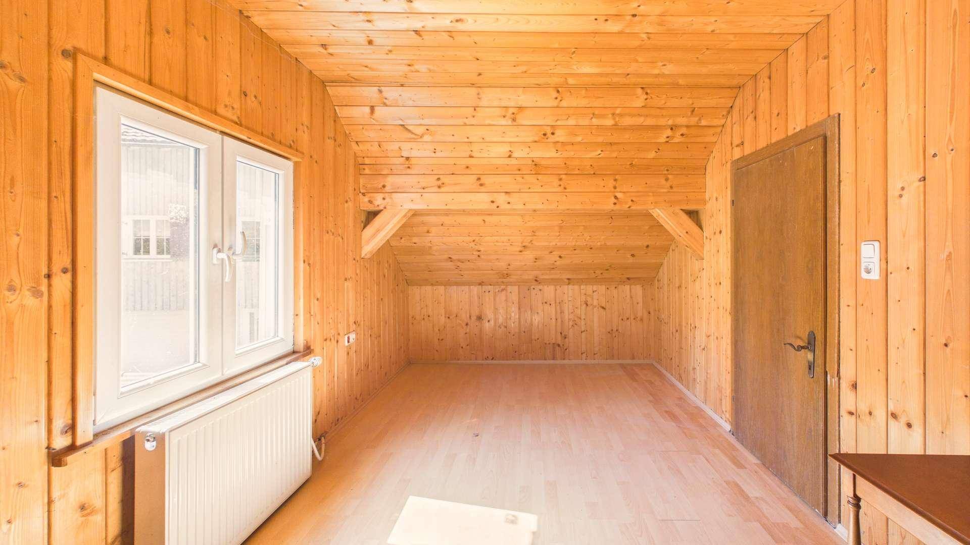 Leerer Dachraum mit Holzverkleidung, Holzbalken und einem Fenster mit Blick nach draußen.