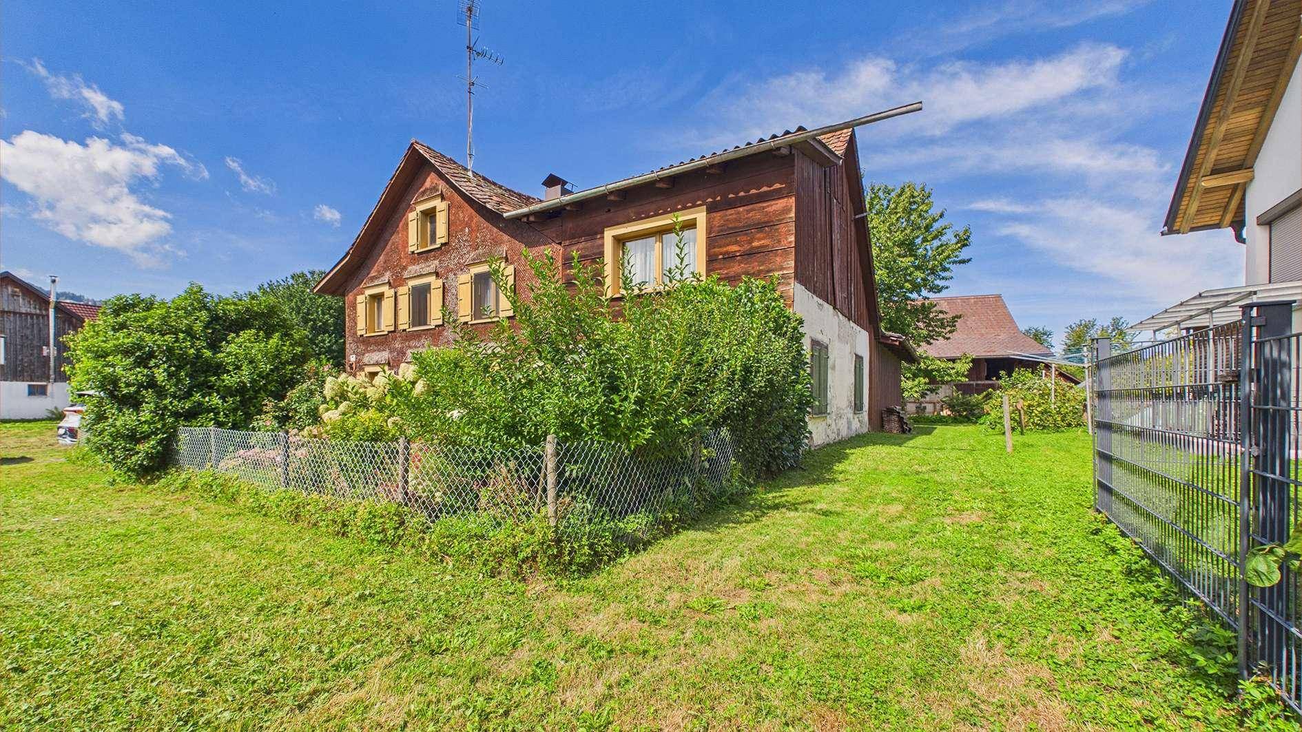 Traditionelles Holzhaus mit gelben Fensterläden und einem gepflegten Gartenbereich.