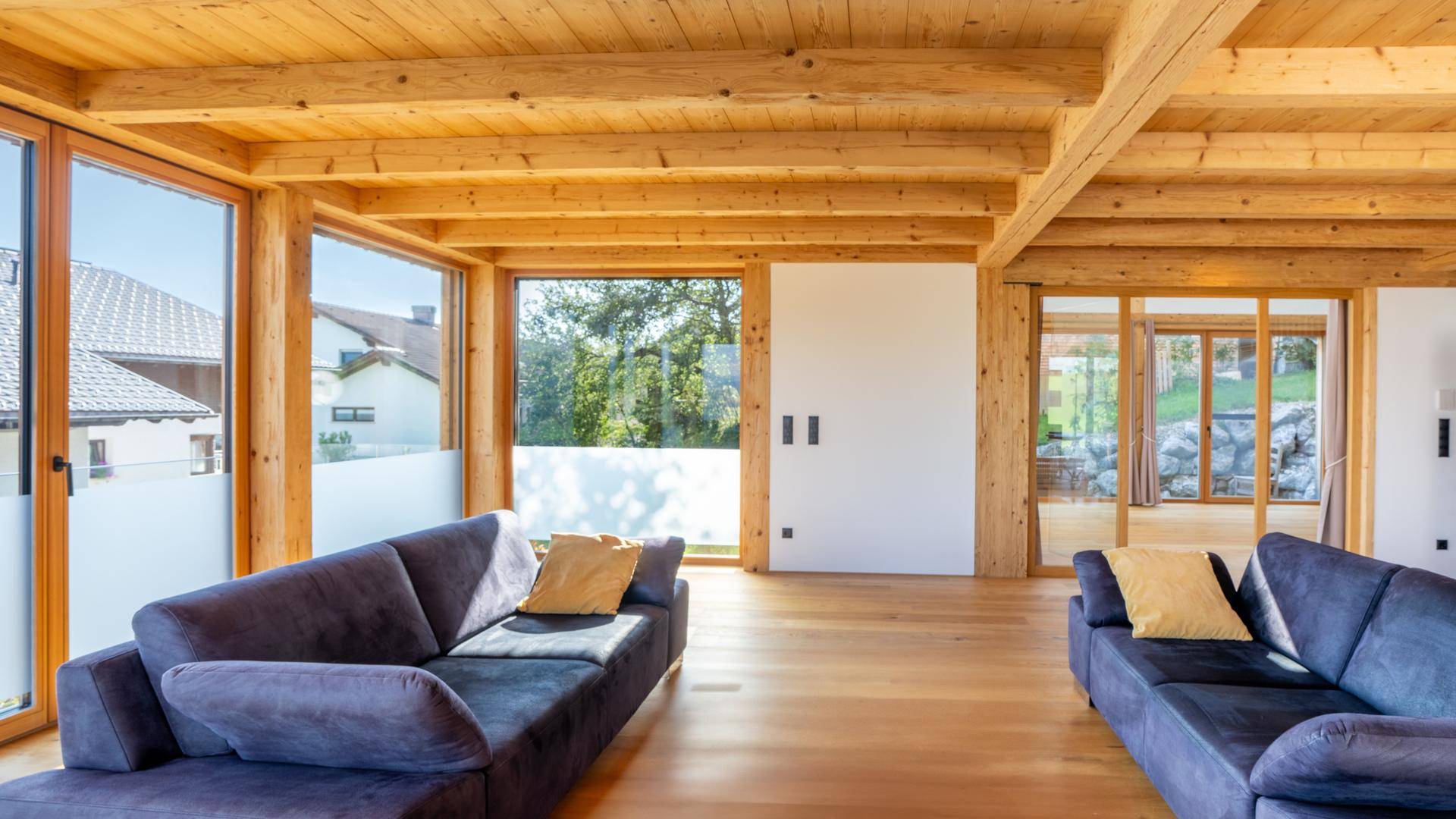 Helles Wohnzimmer mit Holzbalkendecke, großen Fenstern und bequemen Sofas.