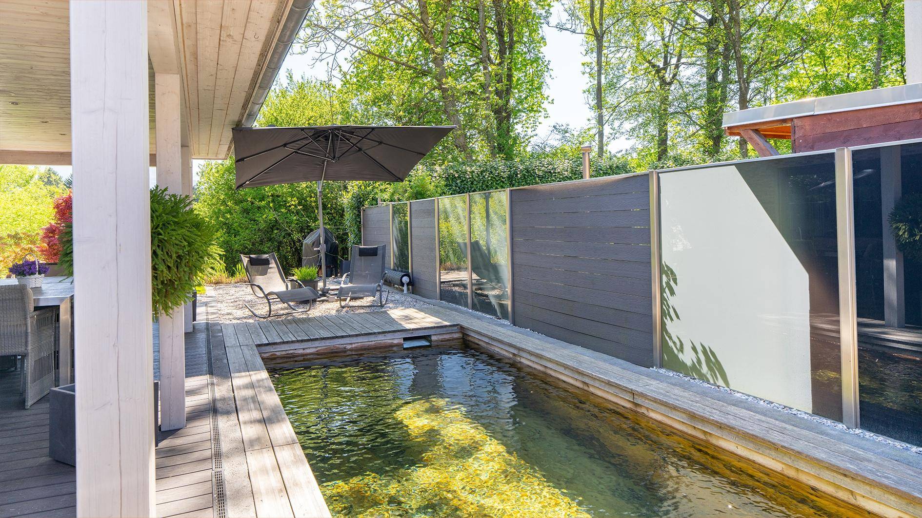 Entspannungsbereich auf der Terrasse mit Liegestühlen, Sonnenschirm und Teich.