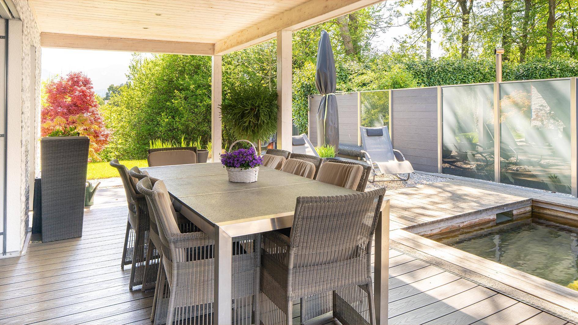 Überdachte Terrasse mit großem Esstisch und Blick auf den Garten und Teich.