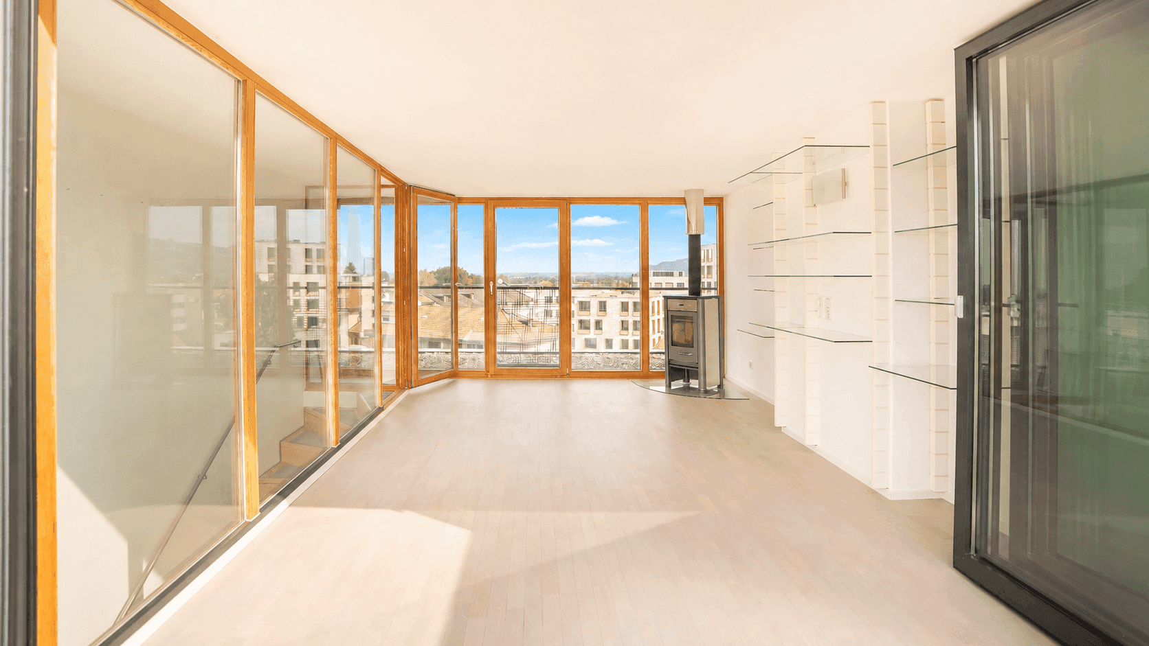 Geräumiges, helles Wohnzimmer mit großen Fenstern, Kaminofen und Panoramablick auf die Stadt und Berge.