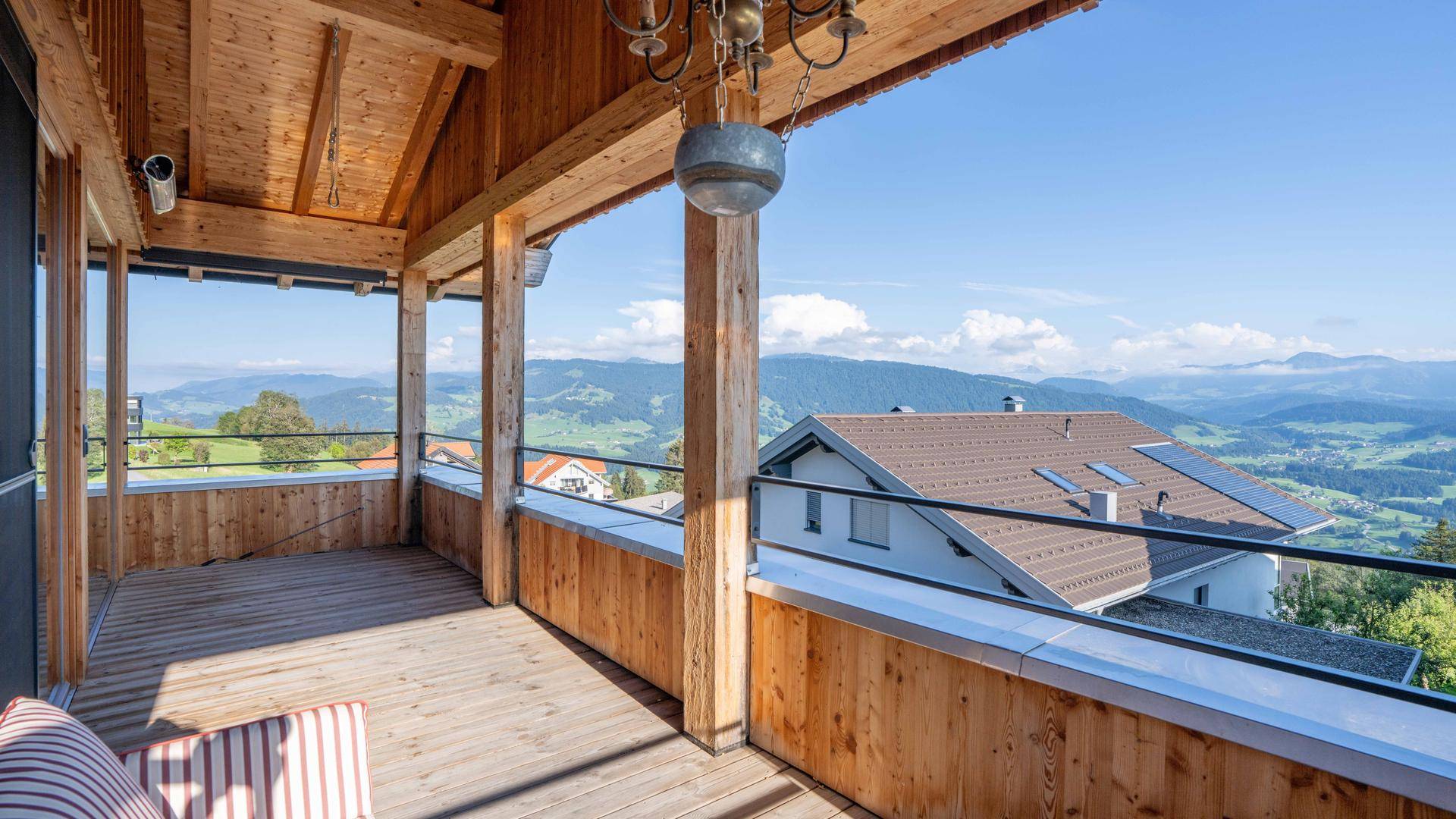 Geräumiger Balkon mit Holzboden und weitem Blick auf die grüne Berglandschaft unter blauem Himmel.