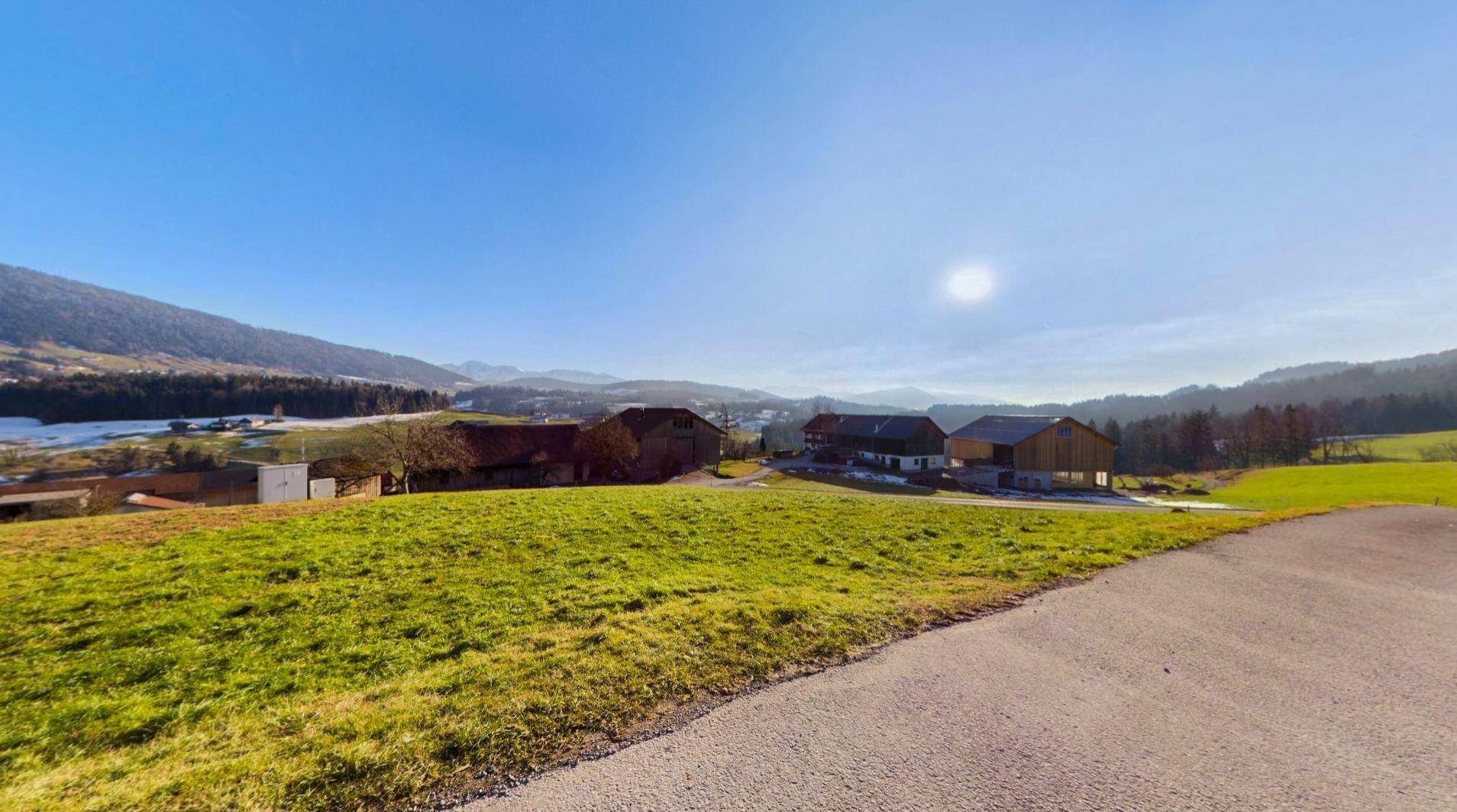 Panoramablick auf die umliegende Landschaft mit grünen Hügeln und fernen Bergen unter blauem Himmel.