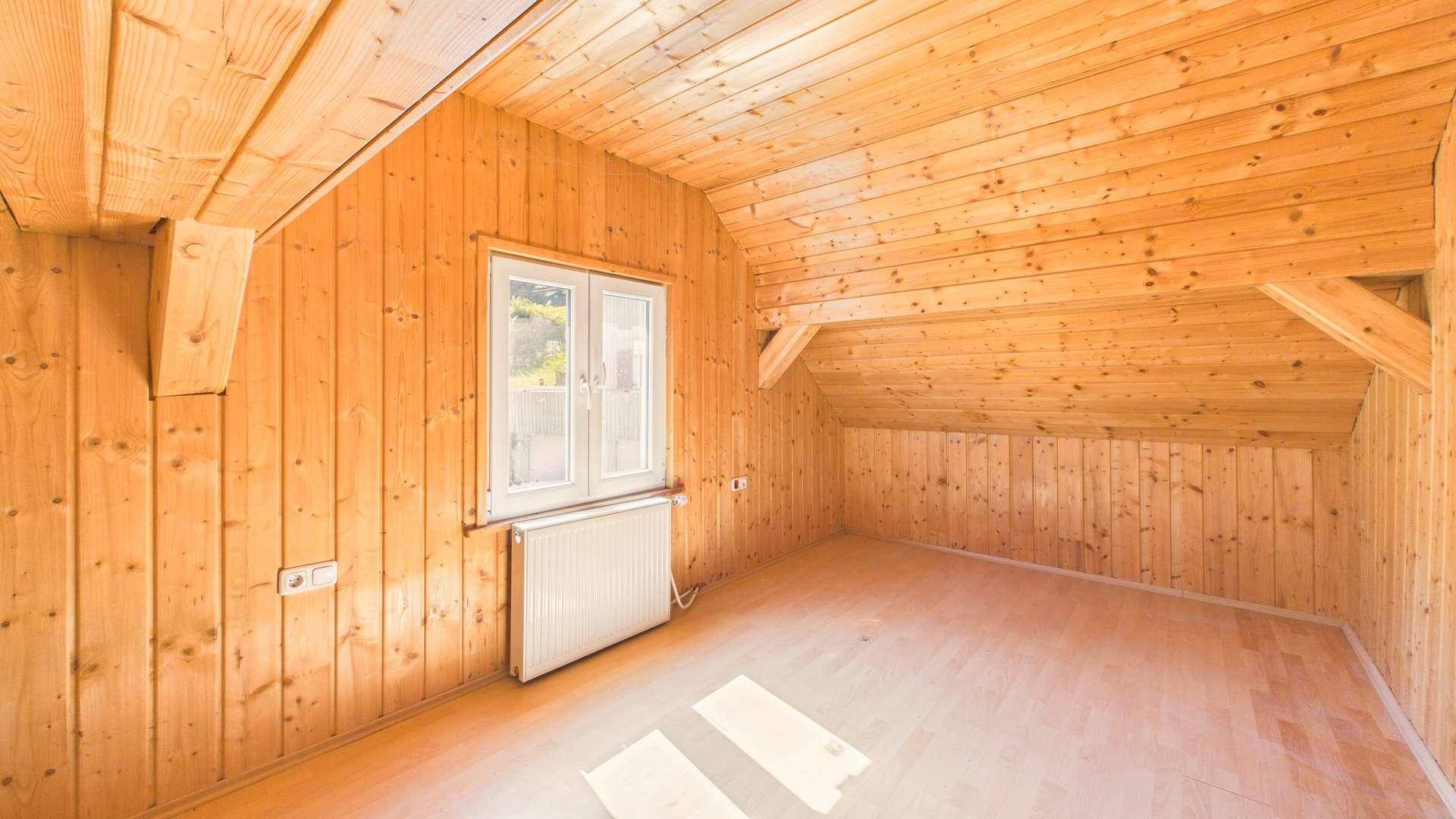 Rustikaler Raum im Dachgeschoss mit Holzverkleidung an Wänden und Decke sowie Fenster.