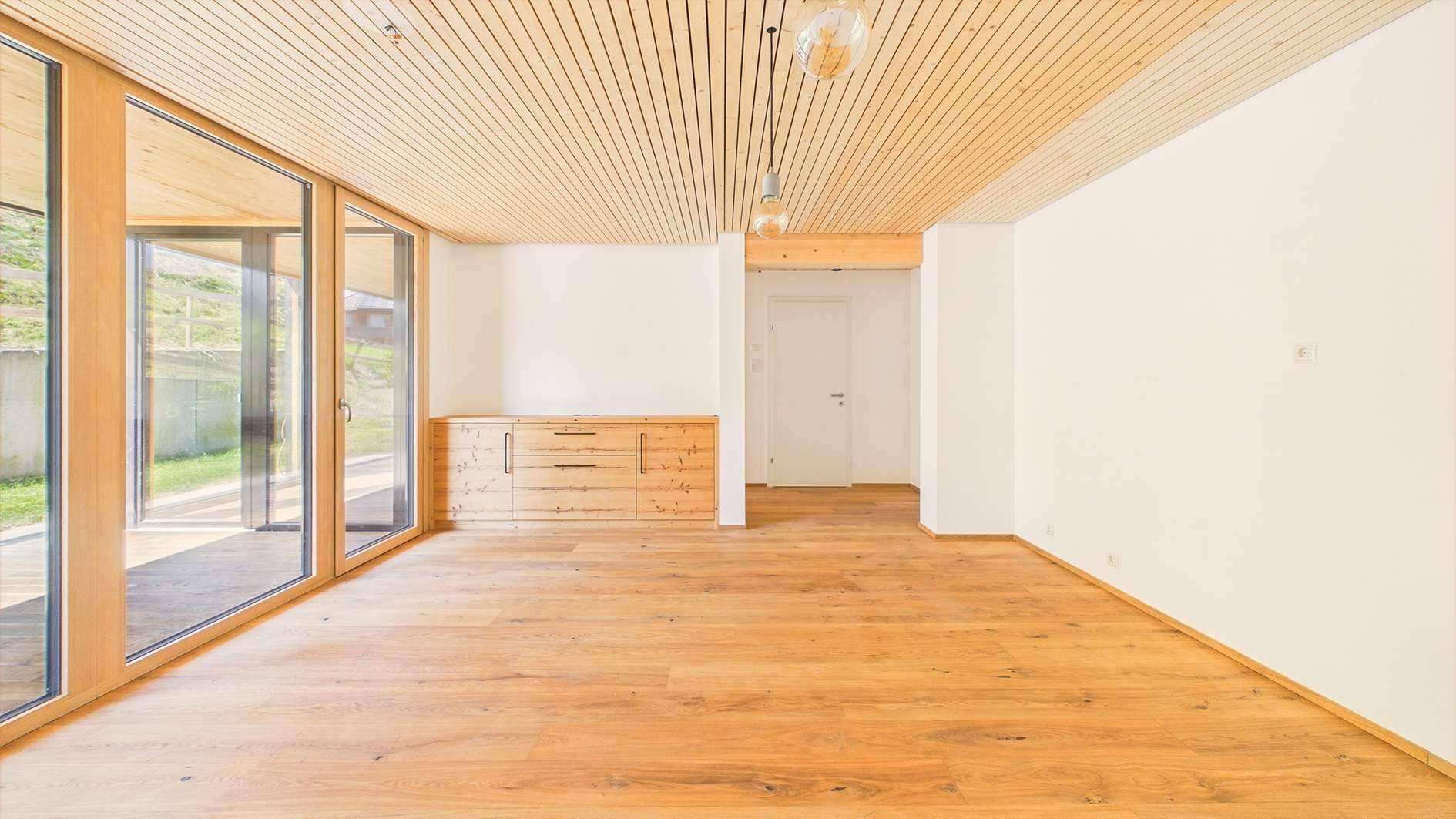 Heller Wohnraum mit Holzboden, Holzlamellendecke und integriertem Holzschrank, bietet Zugang zur Terrasse.