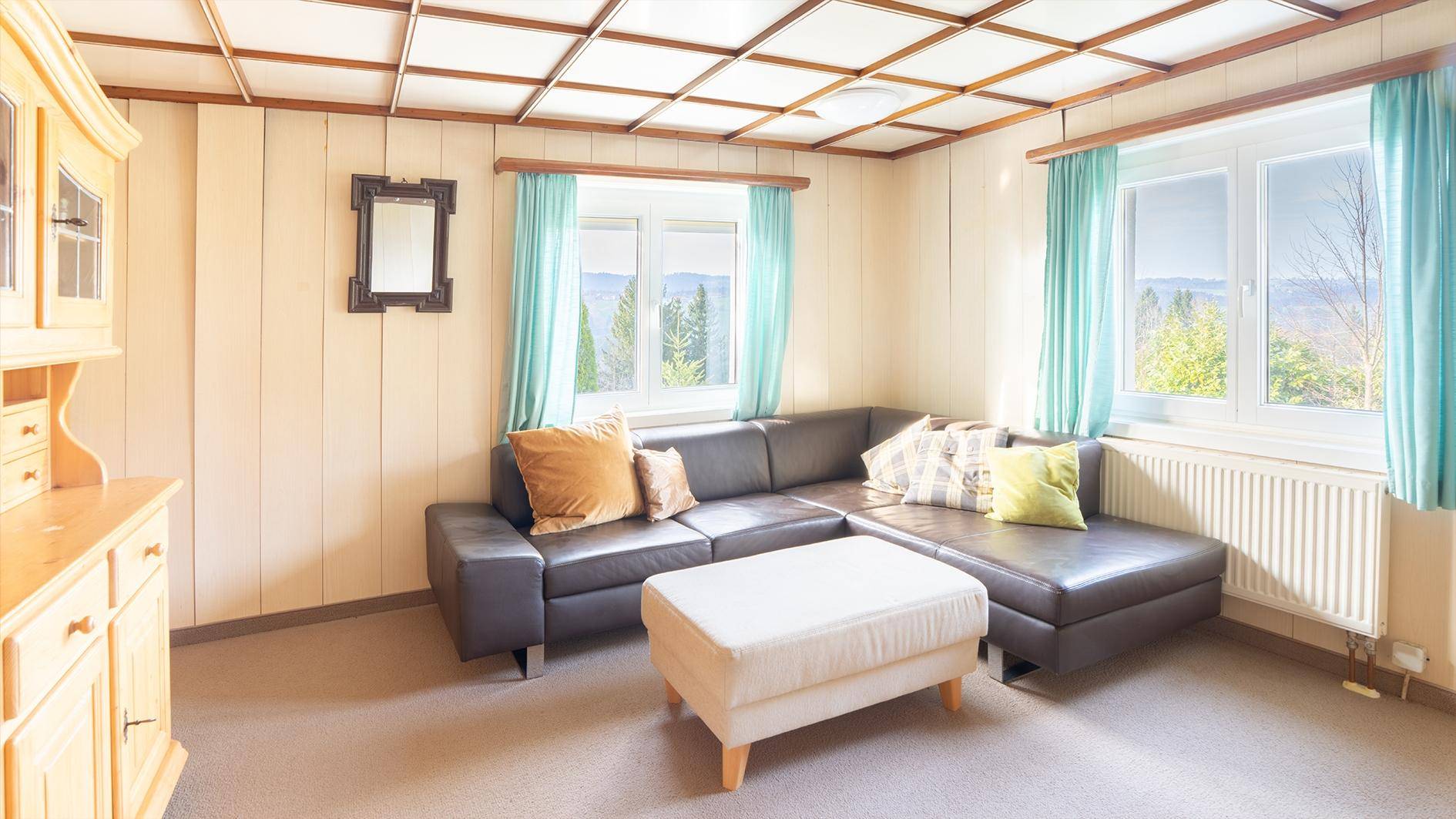Wohnzimmer mit bequemer Eckcouch, Holzdecke und Fenstern mit Blick auf die Natur.