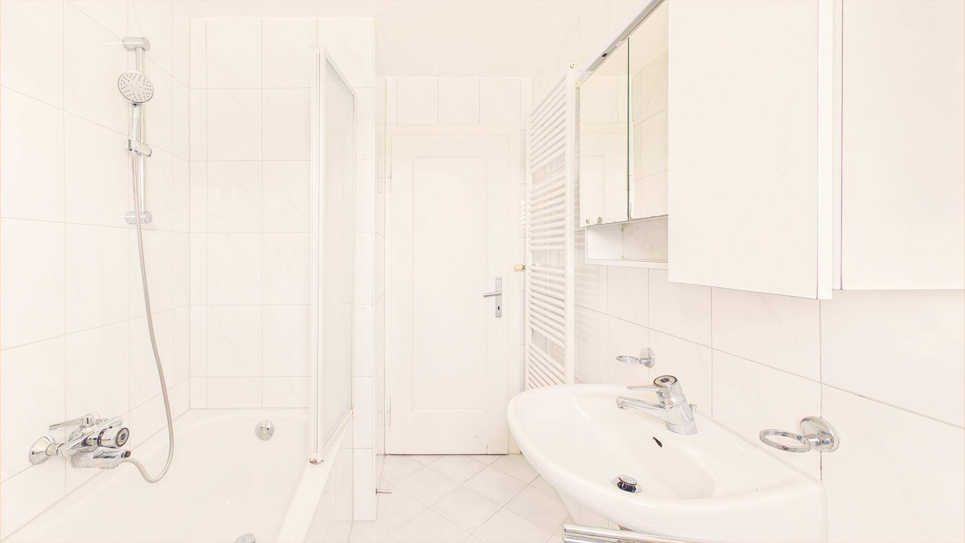 Weiß gefliestes Badezimmer mit Badewanne, Duschvorrichtung und Waschbecken, funktional und hell.
