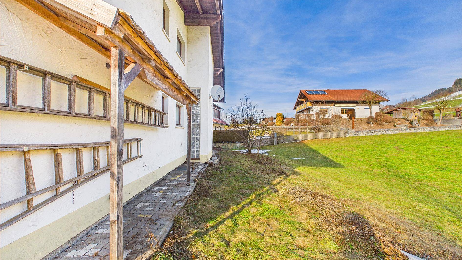 Seitenansicht des Hauses mit gepflastertem Weg und weitläufiger Rasenfläche im Grünen.
