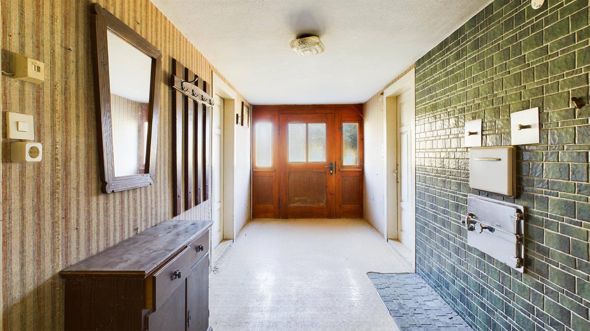 Flur mit gemusterter Tapete, grünen Fliesen an der Wand und einer Holztür im Landhausstil.