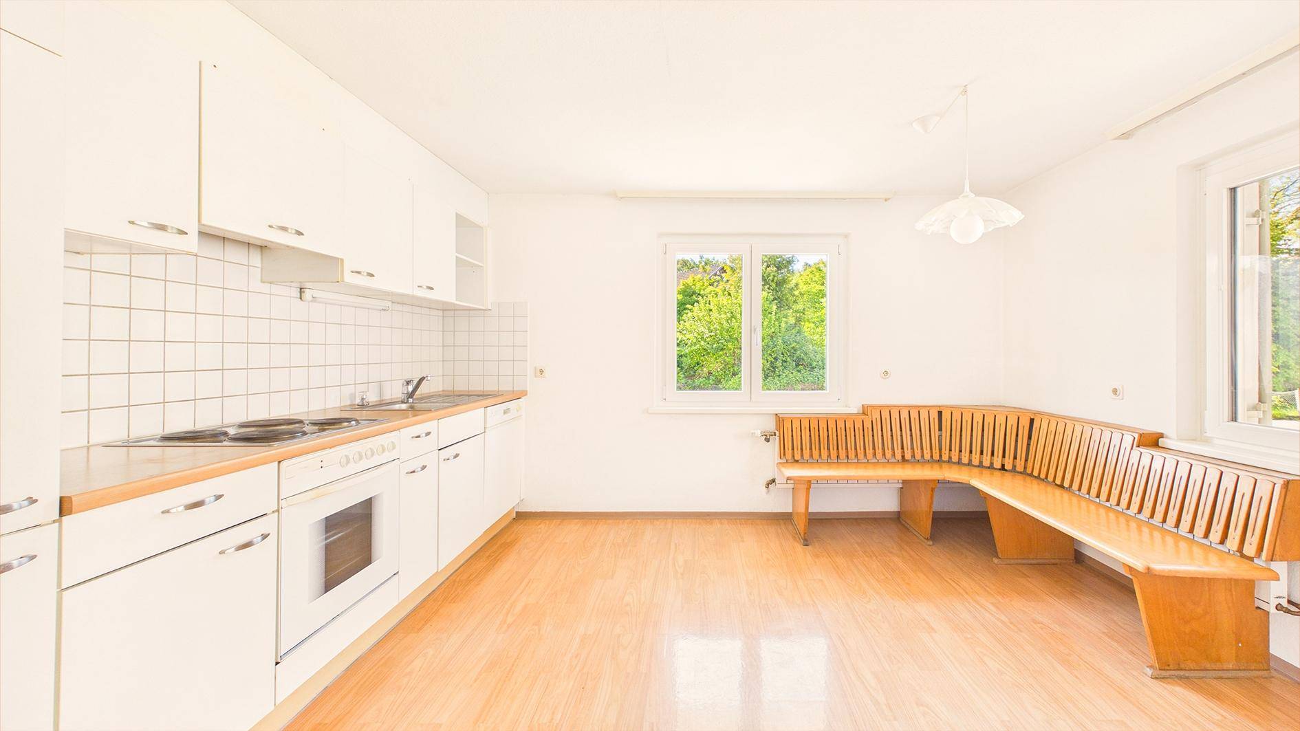 Helle Küche mit weißen Schränken, Holztheke und integrierter Sitzbank, bereit zur Nutzung.