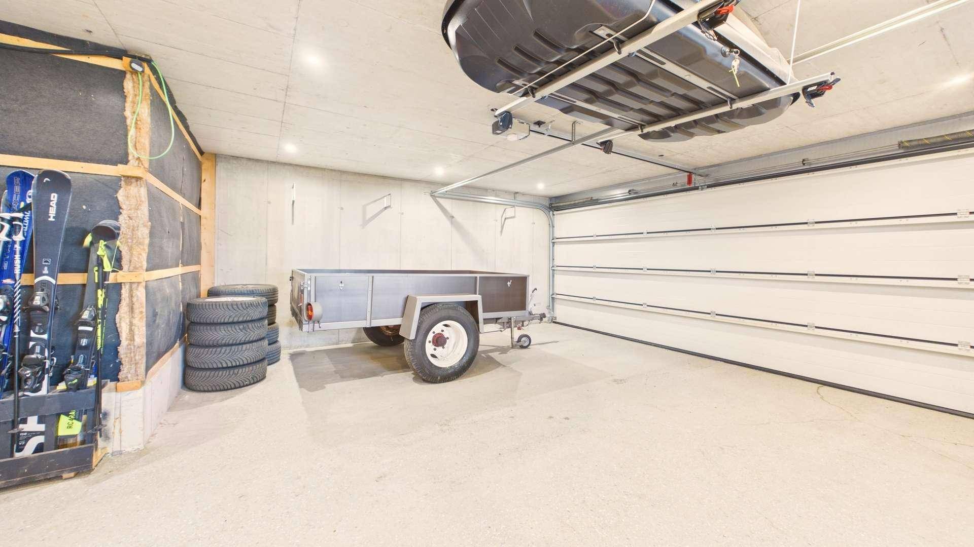 Geräumige Garage mit Betonwänden, einem Anhänger, Reifen und Skiausrüstung.