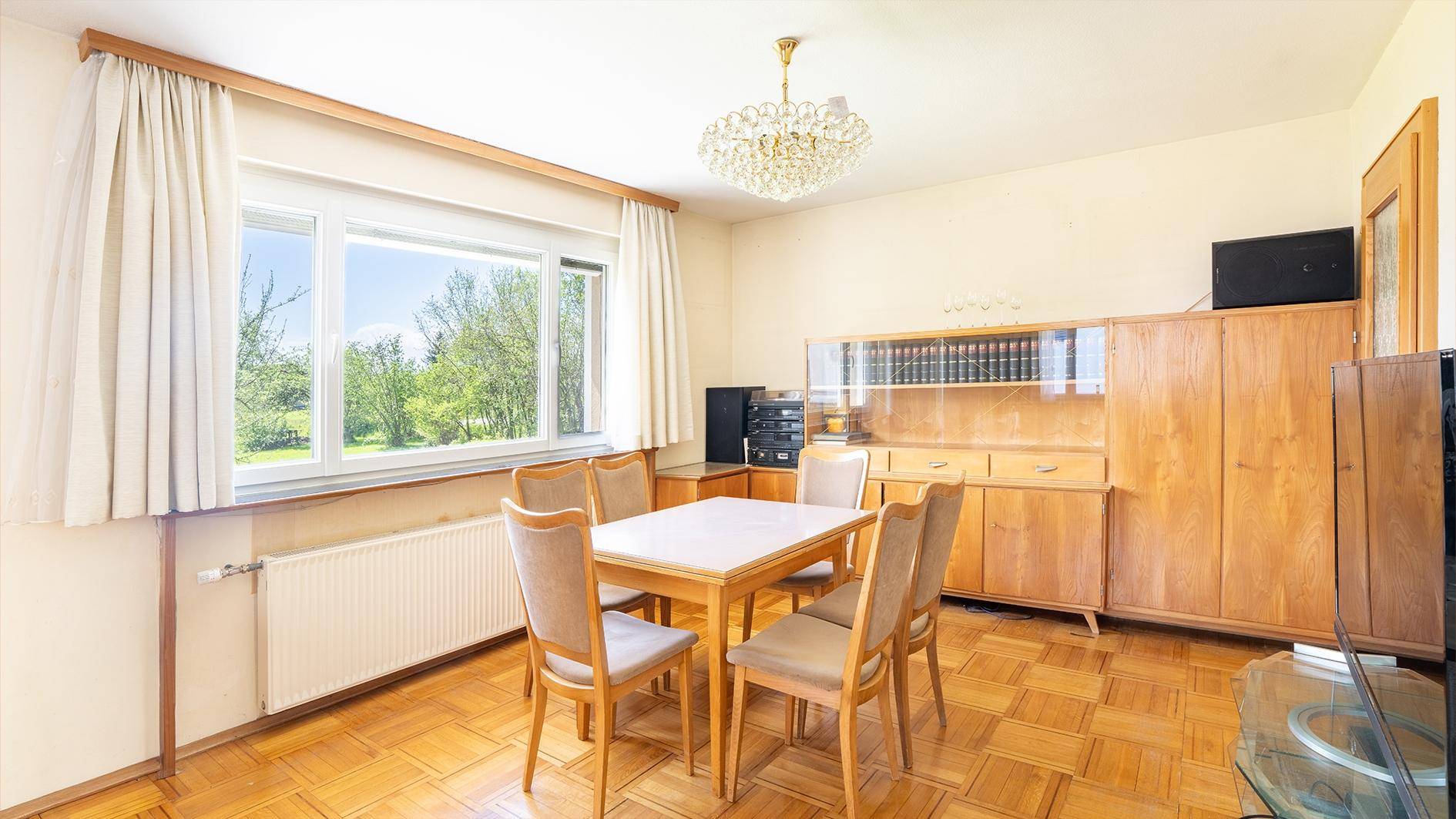 Essbereich mit Holztisch, Stühlen und einem großen Fenster mit Blick ins Grüne.