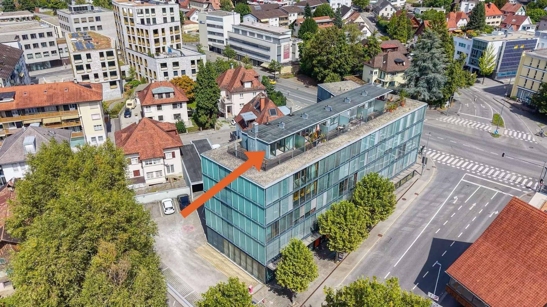 Luftaufnahme eines modernen Gebäudes mit Glasfassade und Dachterrassen in städtischer Umgebung.