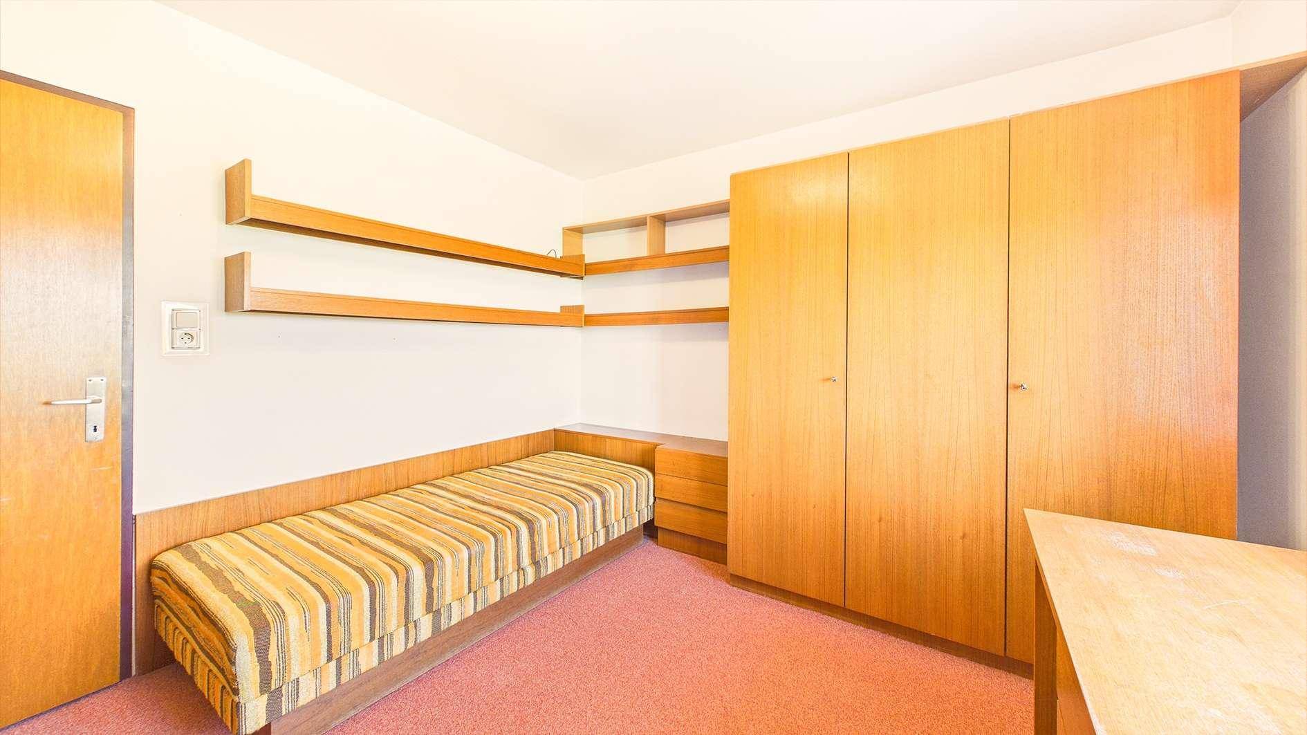 Kinderzimmer oder Büro mit Teppichboden, Bett und Einbauschränken.