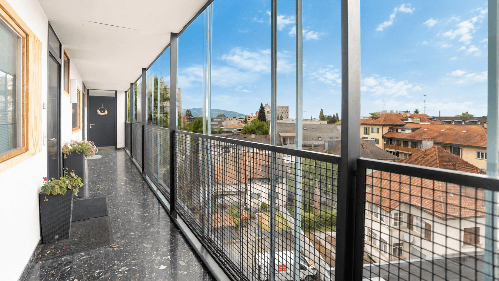 Langer Flur mit dunklem Fliesenboden und weitem Blick über die Stadt durch die Glasfront.