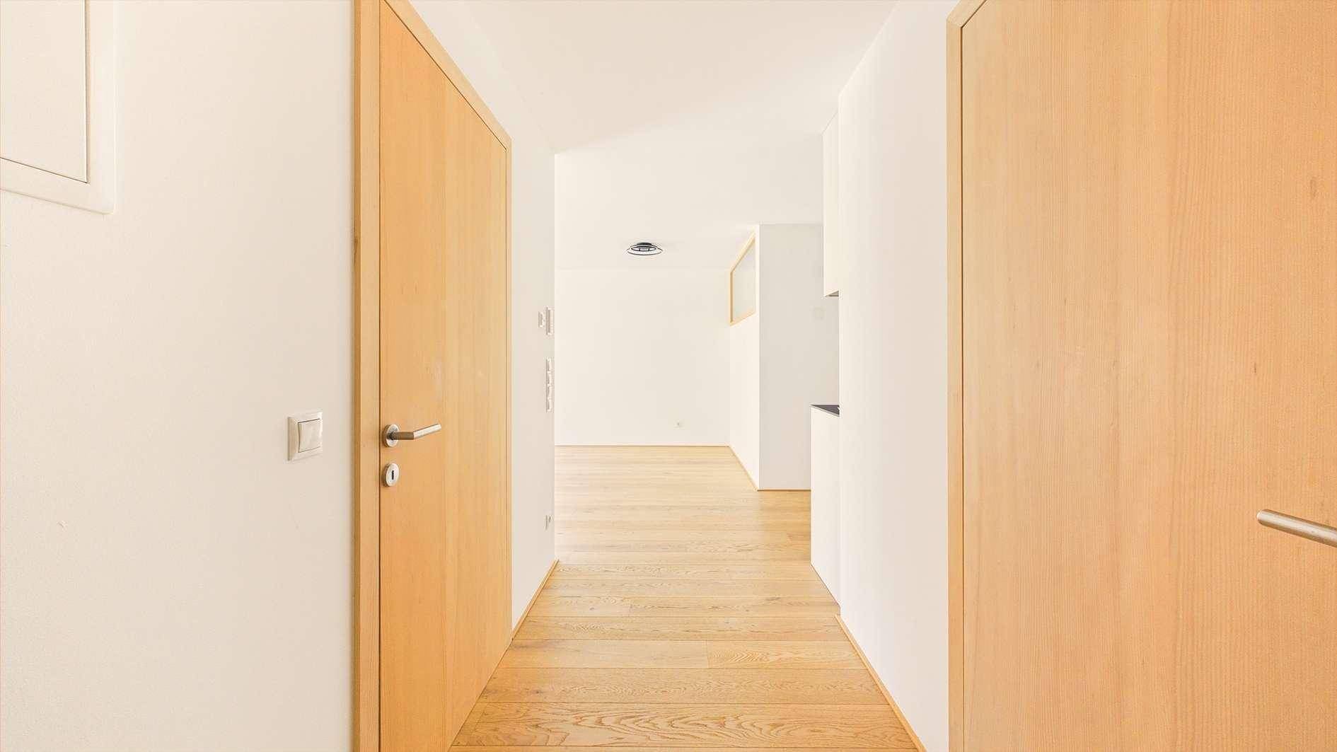 Heller Flur mit Holzboden und Holztüren, der zu den verschiedenen Räumen führt.