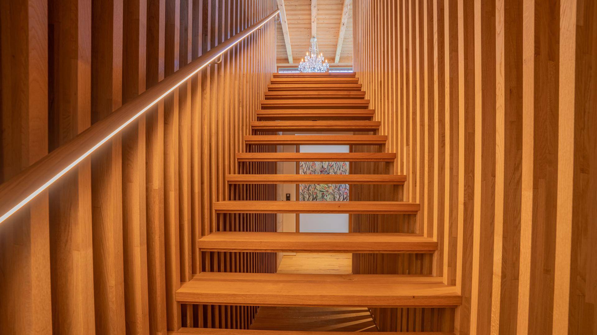 Elegante Holztreppe mit integrierter Beleuchtung und vertikalen Holzlamellen als Geländer.