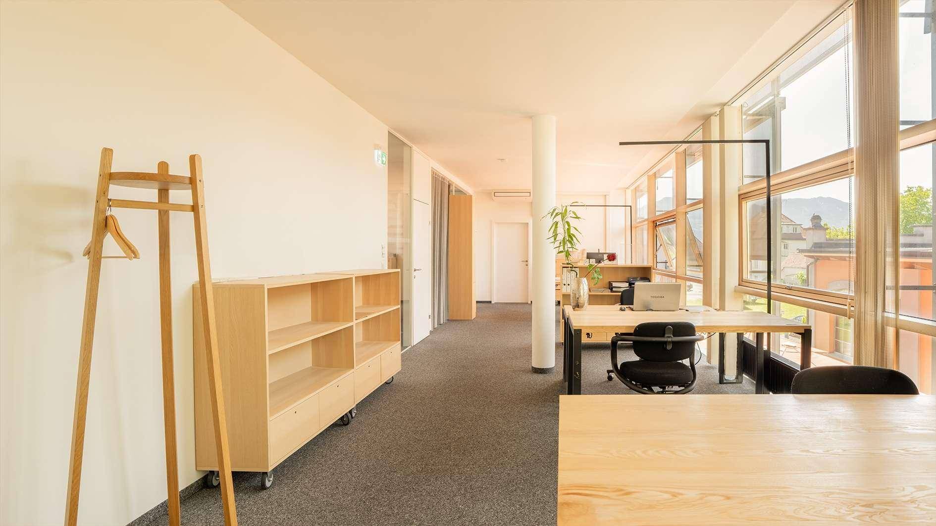Helles, modernes Büro mit großen Fenstern, Holztischen und Teppichboden, bietet viel natürliches Licht.