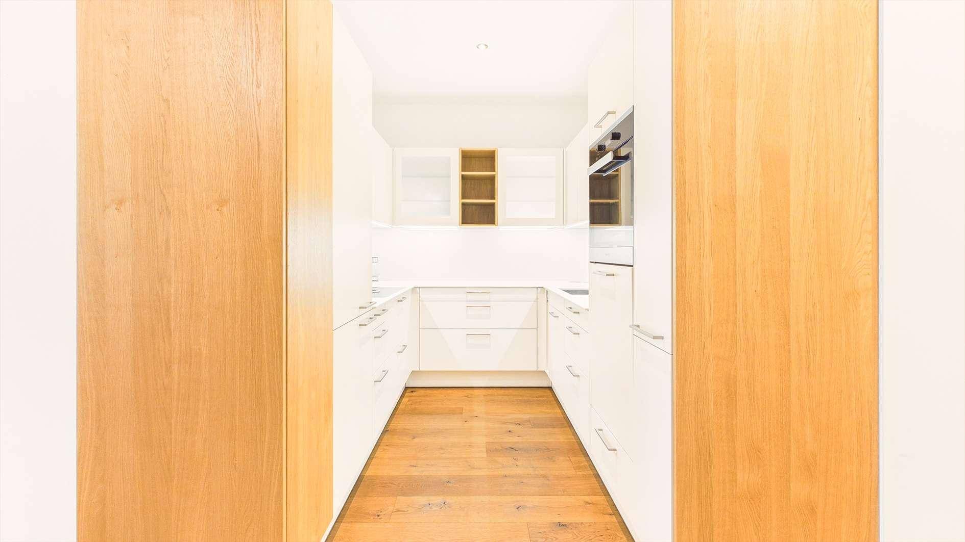 Moderne weiße Küche mit Holzboden und integrierten Geräten.