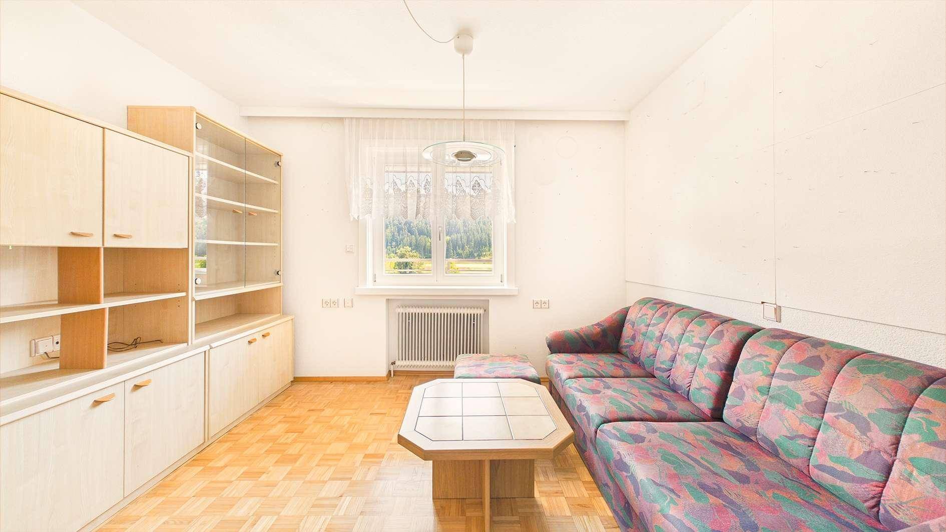 Wohnzimmer mit Parkettboden, Schrankwand und Fenster mit Blick auf die Natur.