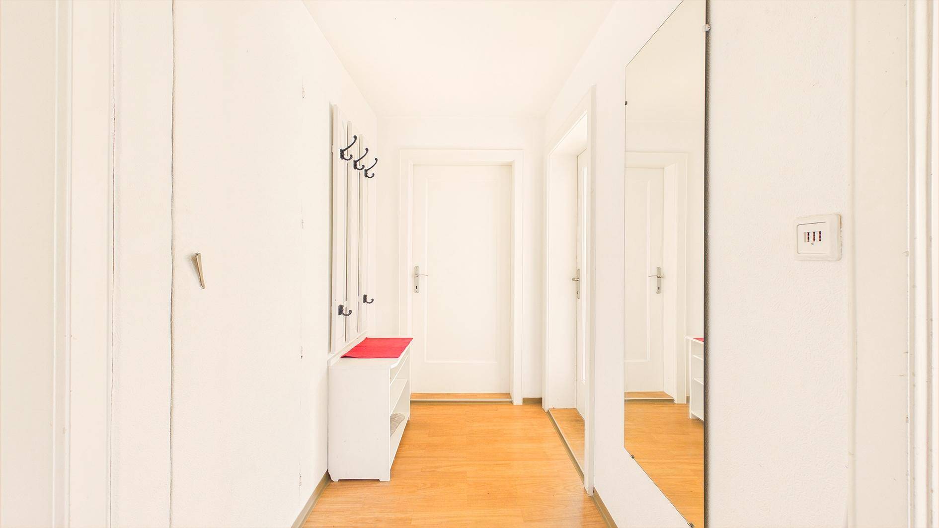 Heller Eingangsbereich mit Parkettboden, Spiegel und Garderobe, einladend und funktional.