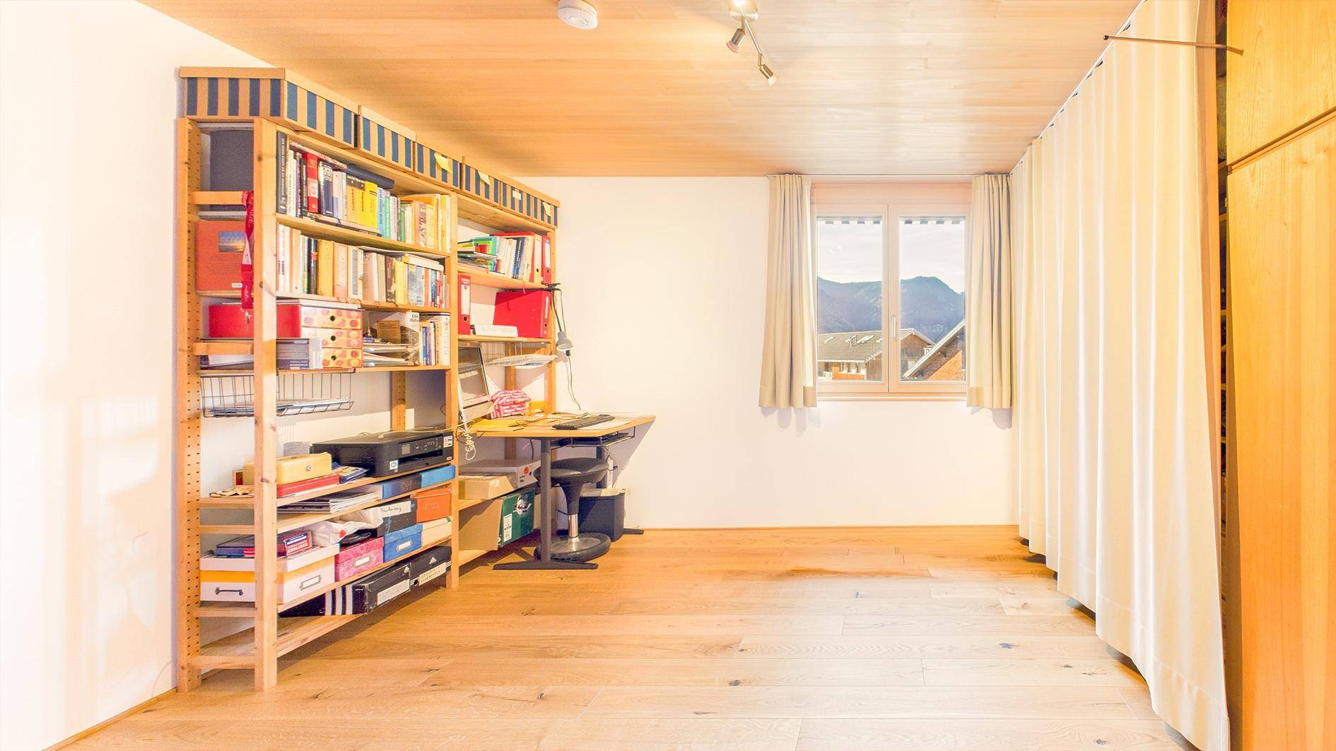 Helles Arbeitszimmer mit Holzboden, Bücherregal und Fenster mit Bergblick.